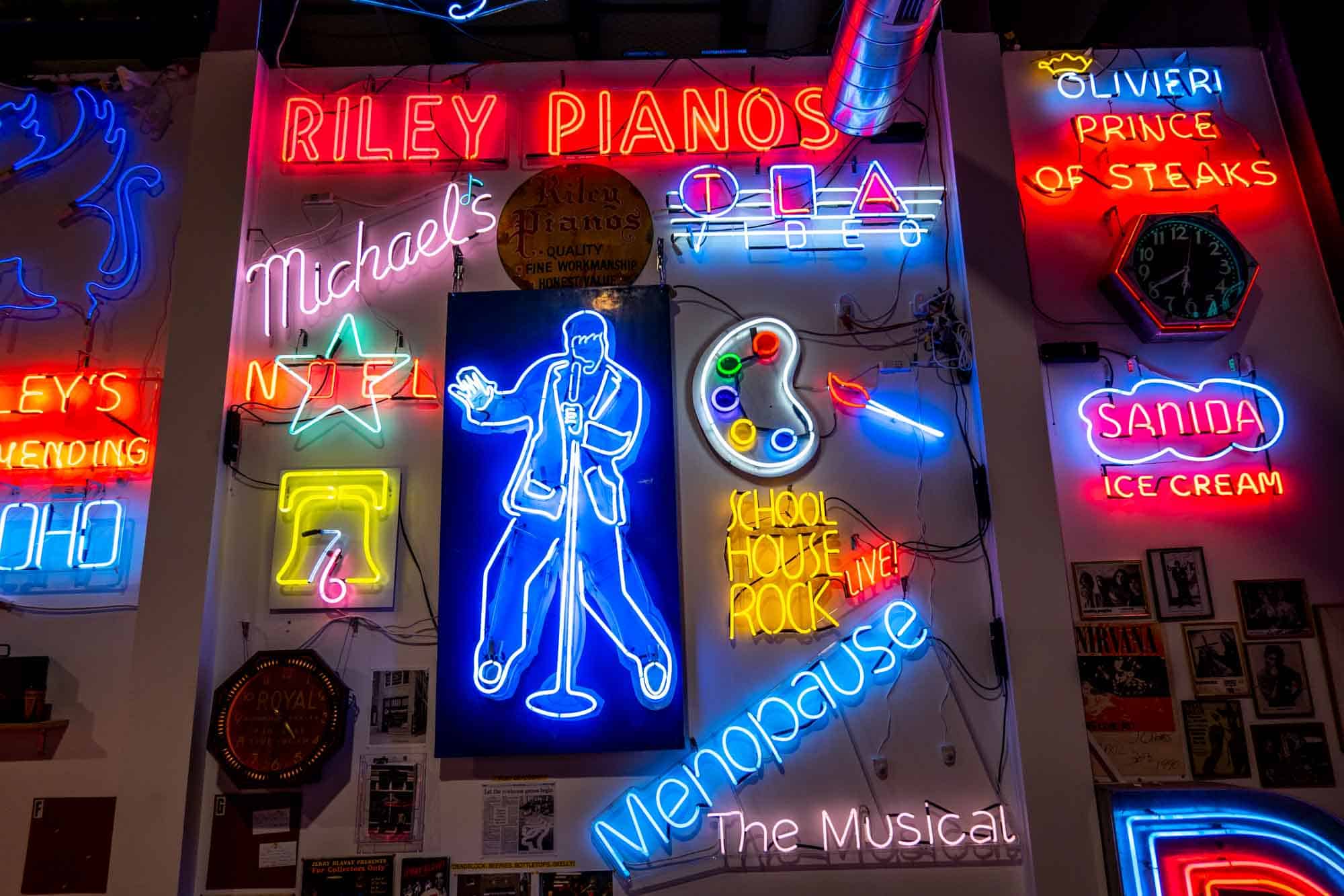 Colorful neon signs on a wall, including an image of Elvis, a painters' palette, and "School House Rock Live!"
