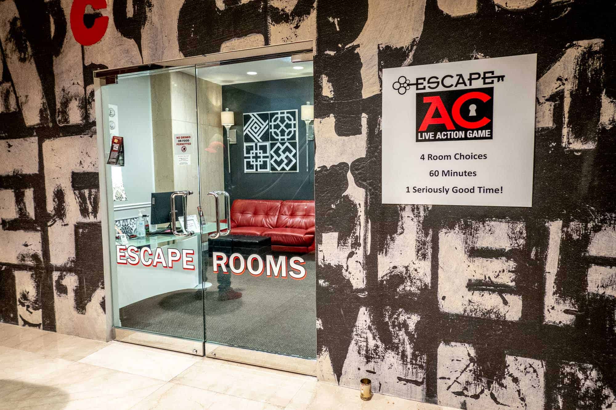 Glass doors in the middle of black and white walls with a sign: "Escape AC: Live Action Game. 4 room choices, 60 minutes, 1 seriously good time!"