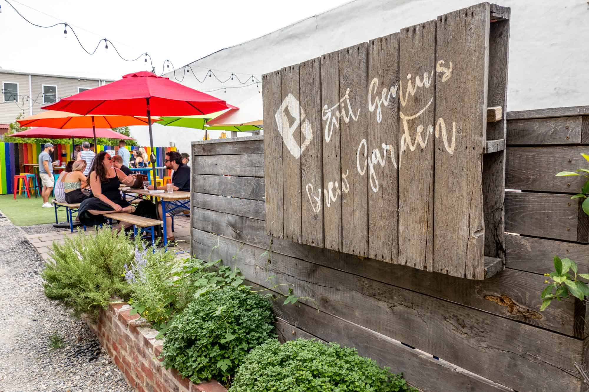 Sign reading "Evil Genius beer garden" in front of tables with colorful umbrellas.