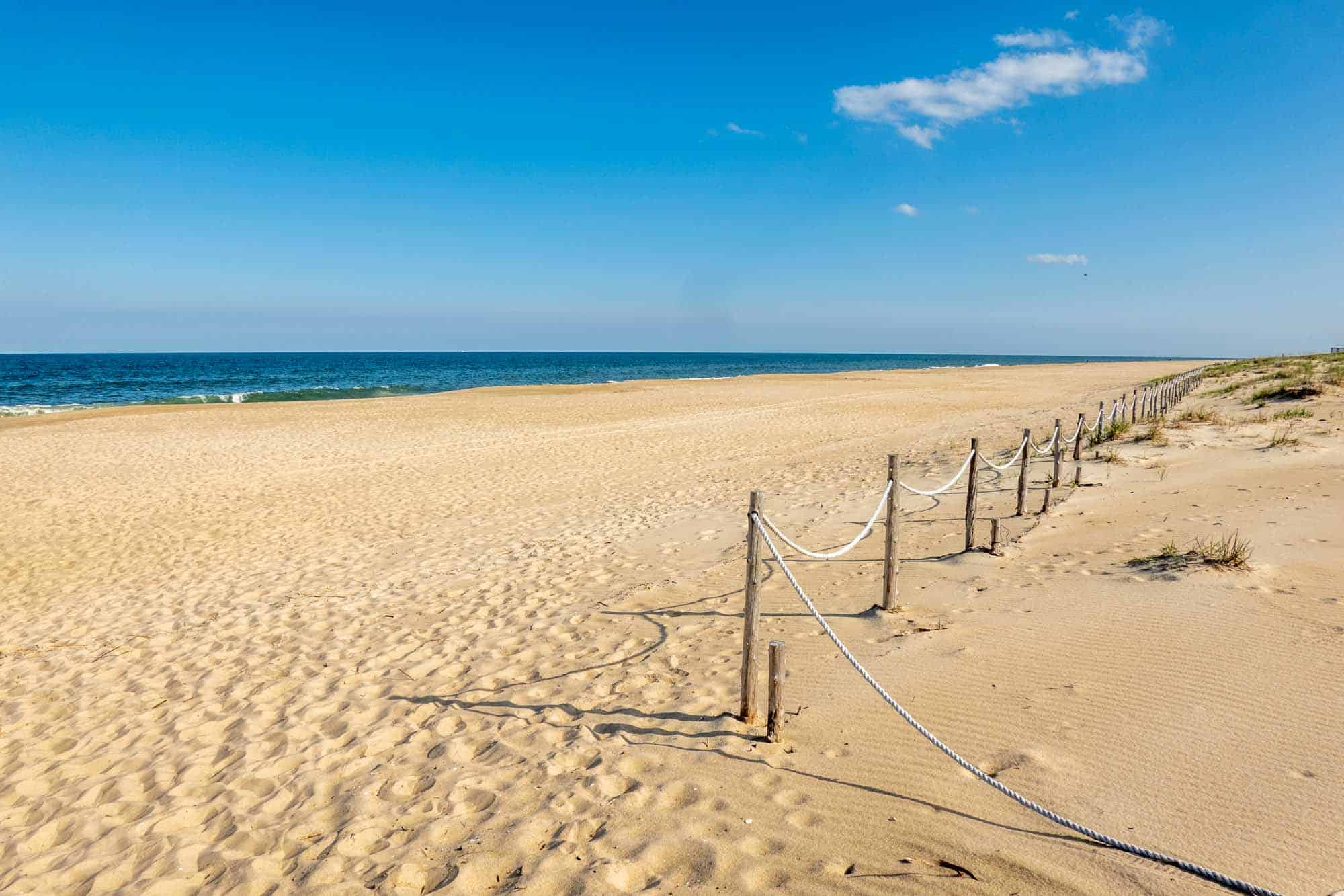 Rope barrier along a golden sand beach beside blue ocean waves.