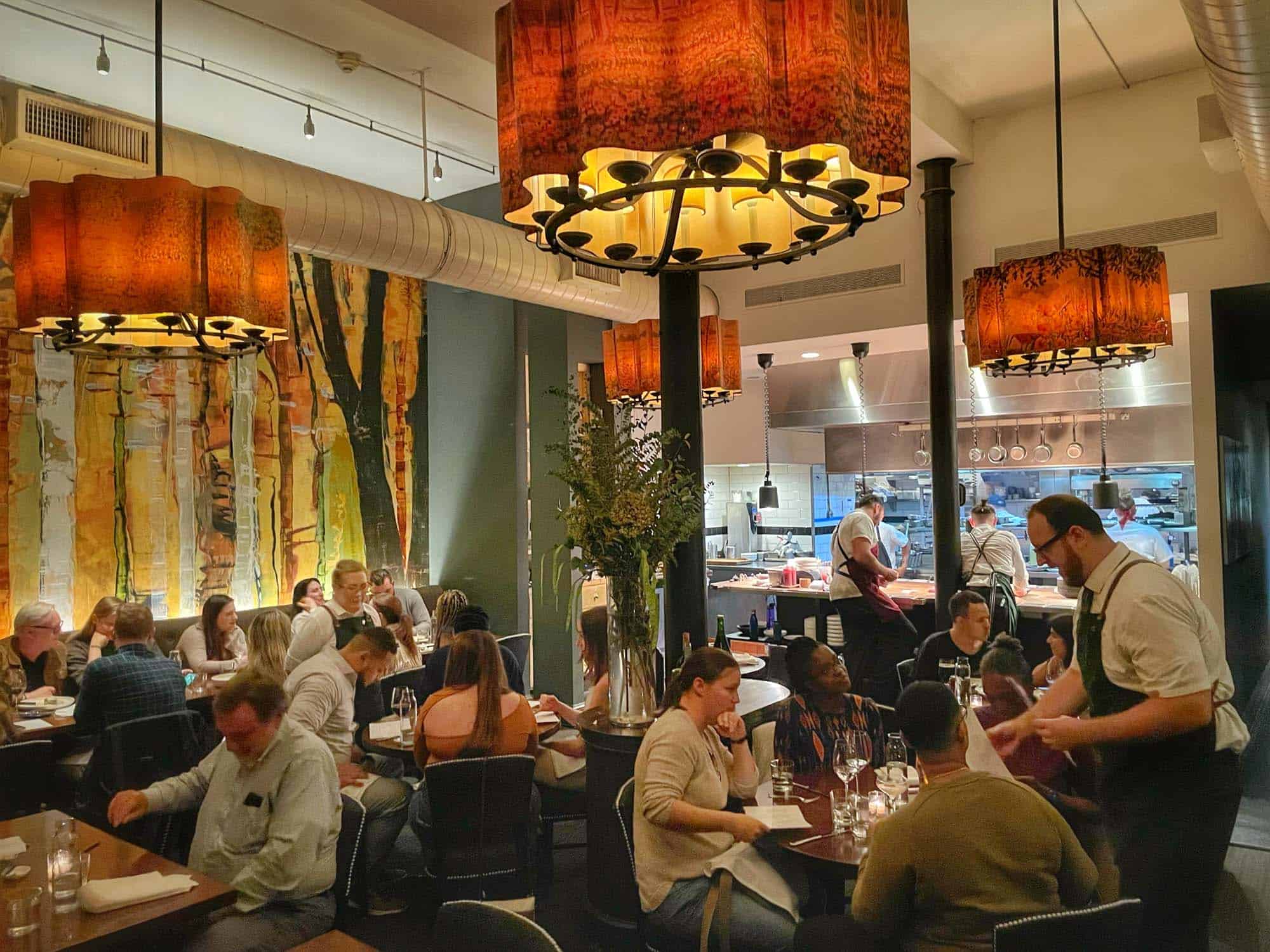 People seated in a restaurant dining room with yellow and green paintings on the wall.