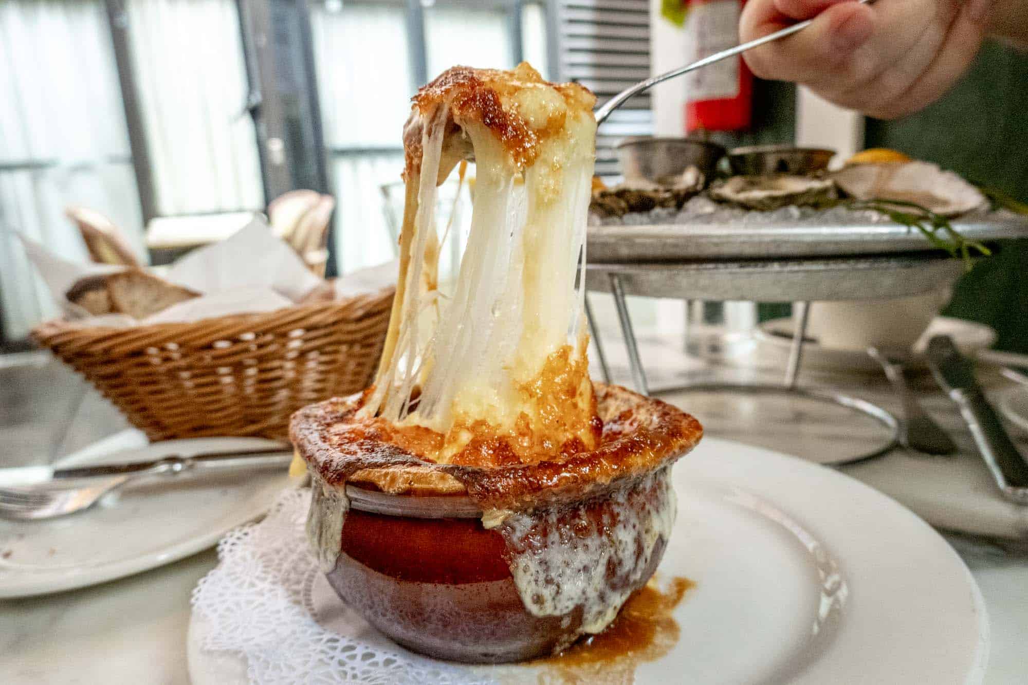 Soup bowl topped with melted cheese pulled up by a spoon.