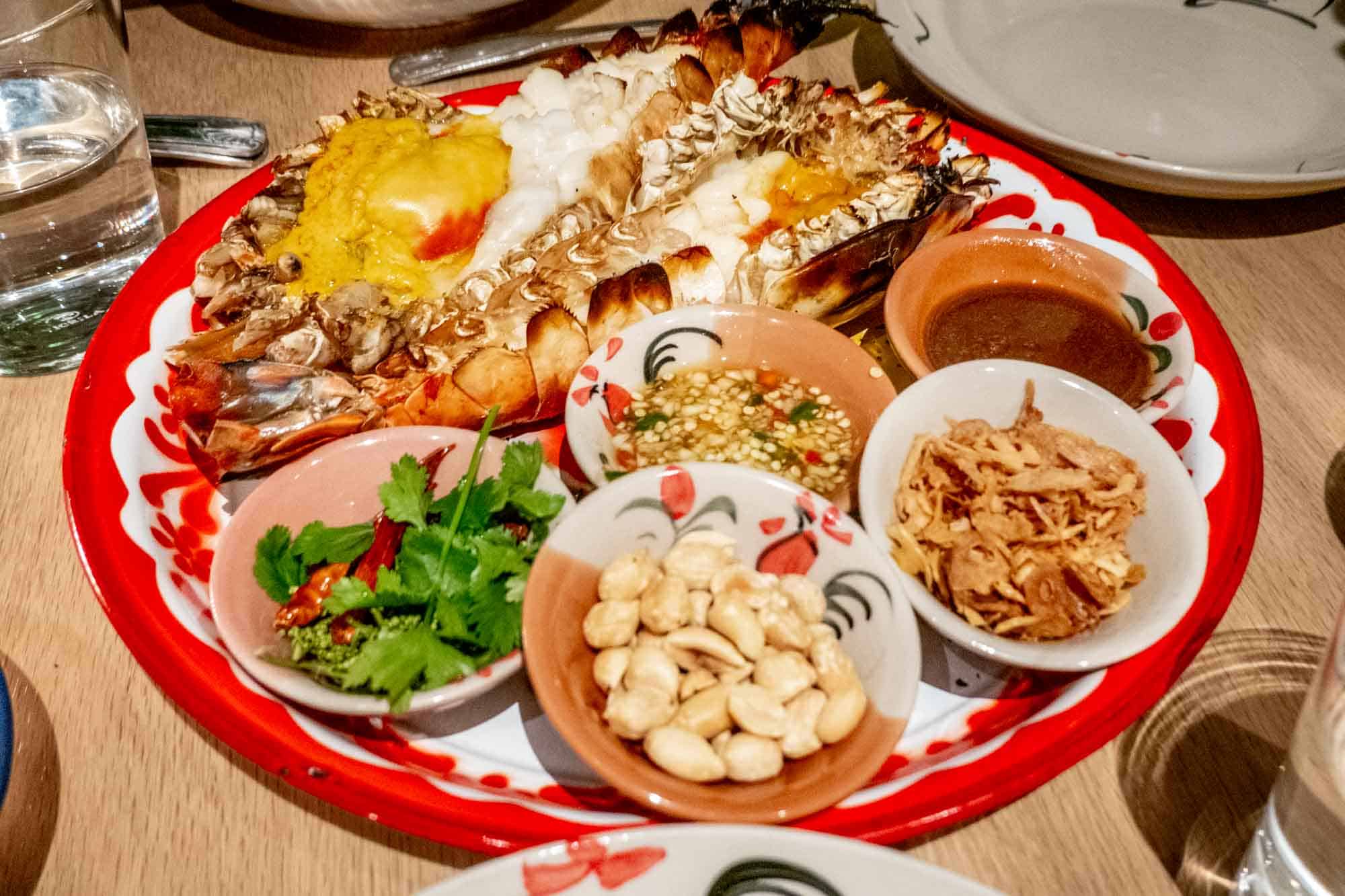 Platter with grilled prawn, peanuts, herbs, and sauces.