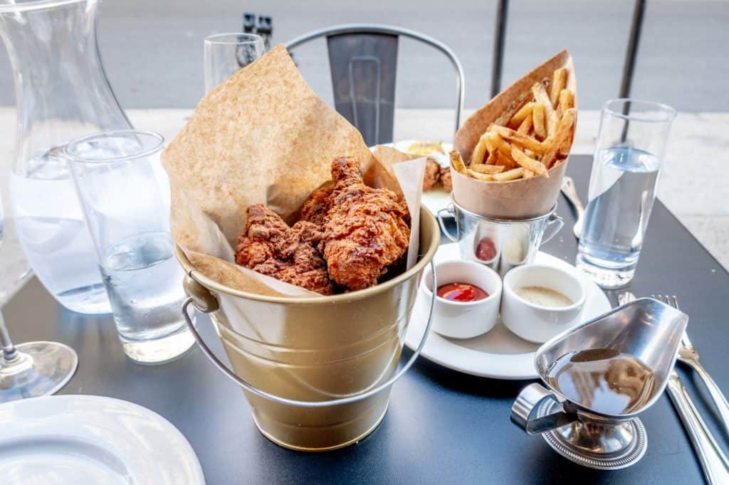 Bucket of fried chicken, French fries, and sauces on an outdoor restaurant table at Bar Poulet