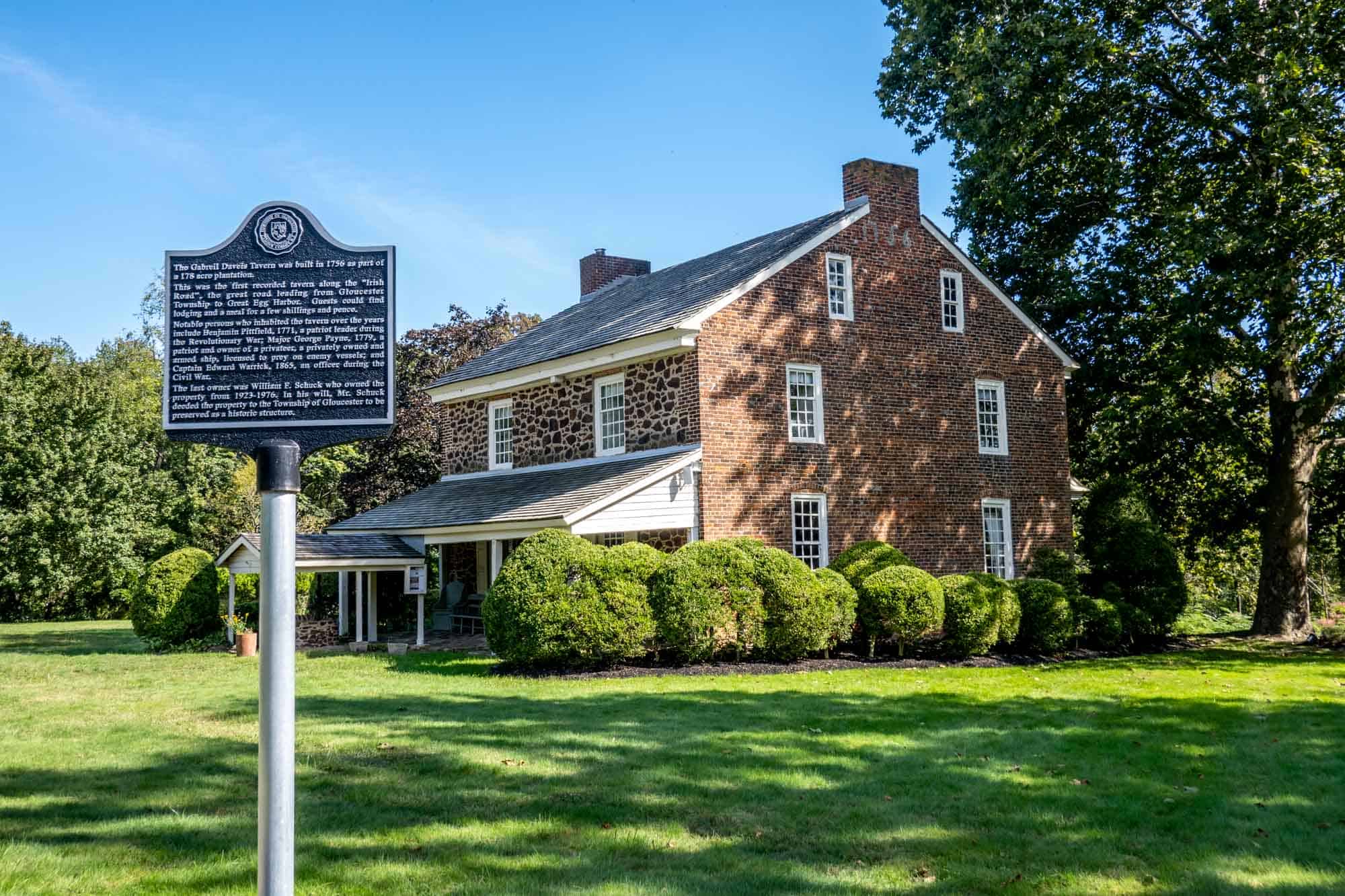 two-story brick and stone building with a porch beside an historical marker sign