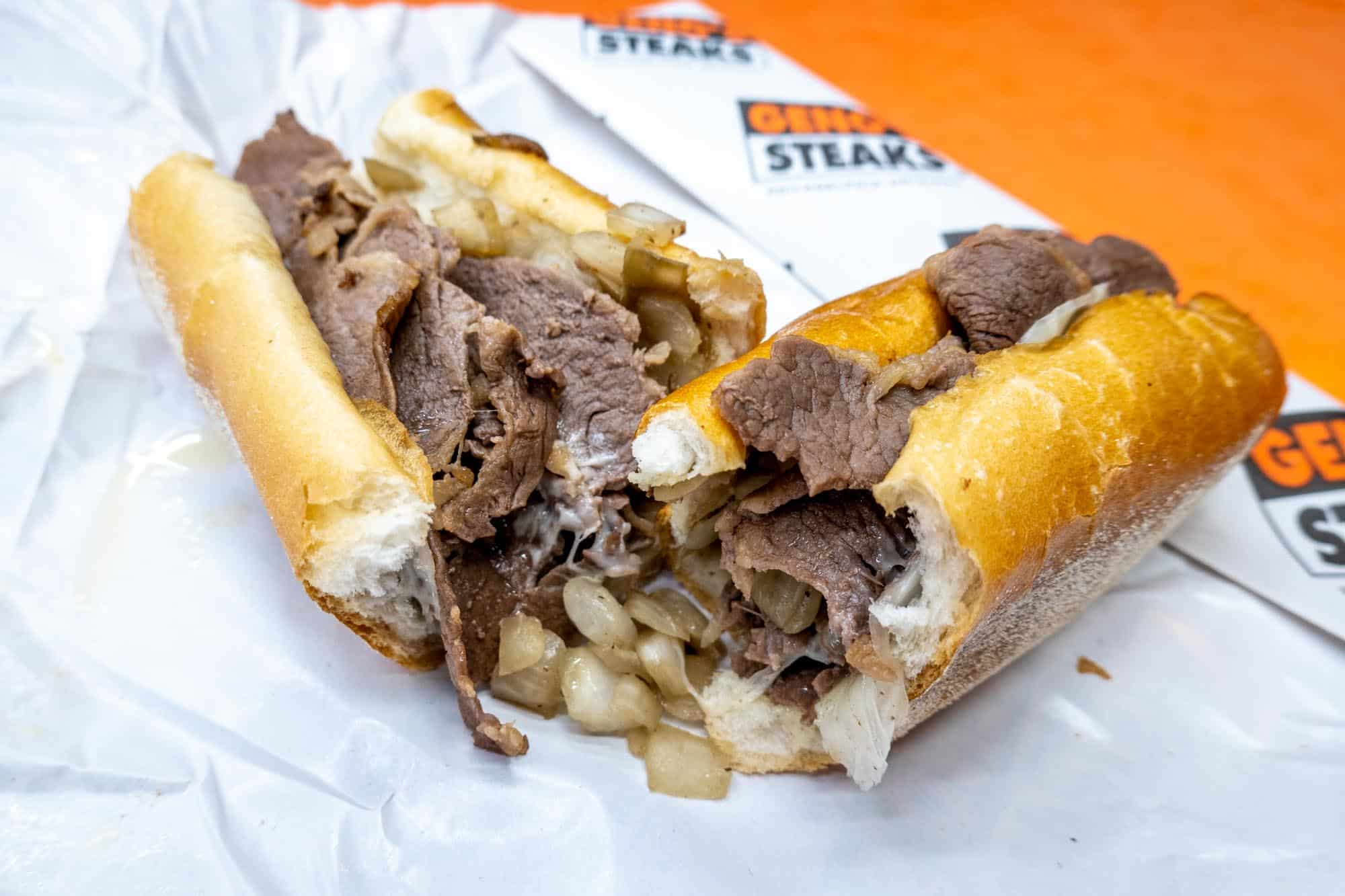 Cheesesteak cut in half on paper wrapper from Geno's Steaks.