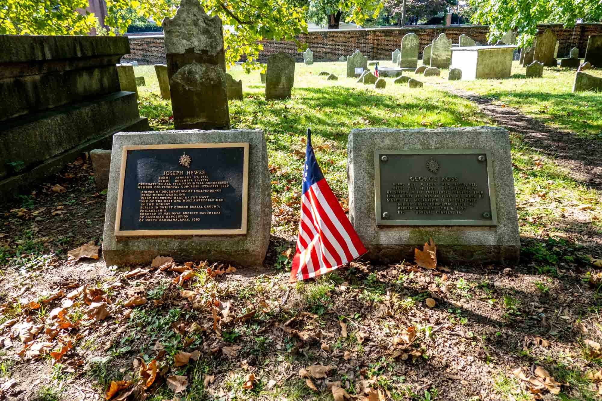 Two headstones with plaques for Joseph Hewes and George Ross with a Colonial flag