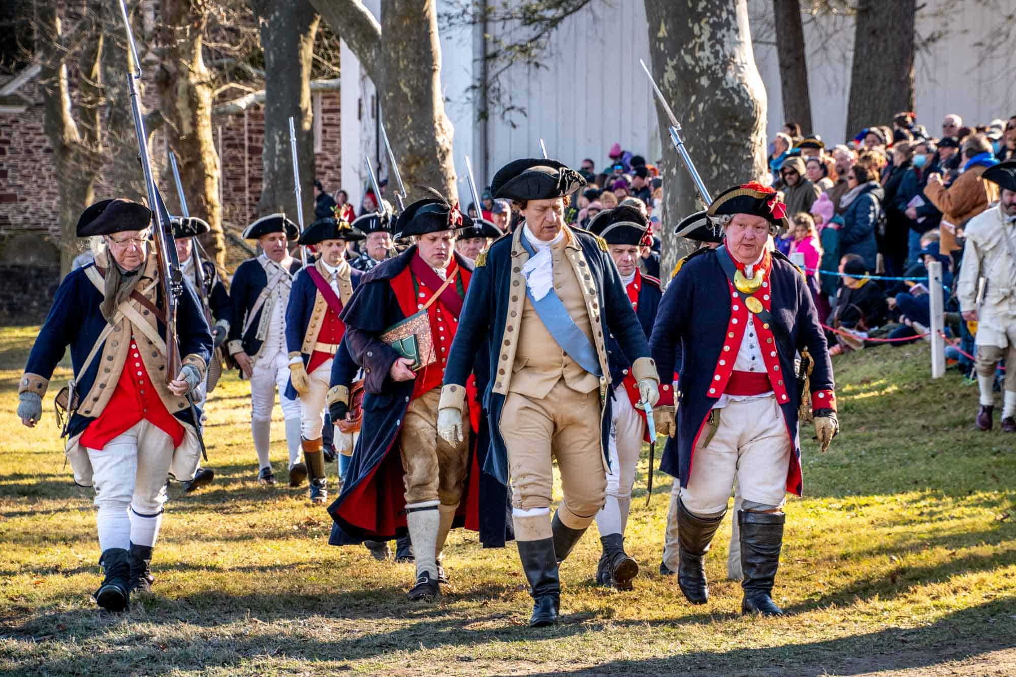 Reenactors in Revolutionary War uniforms, including George Washington, marching at the Washington Crossing reenactment