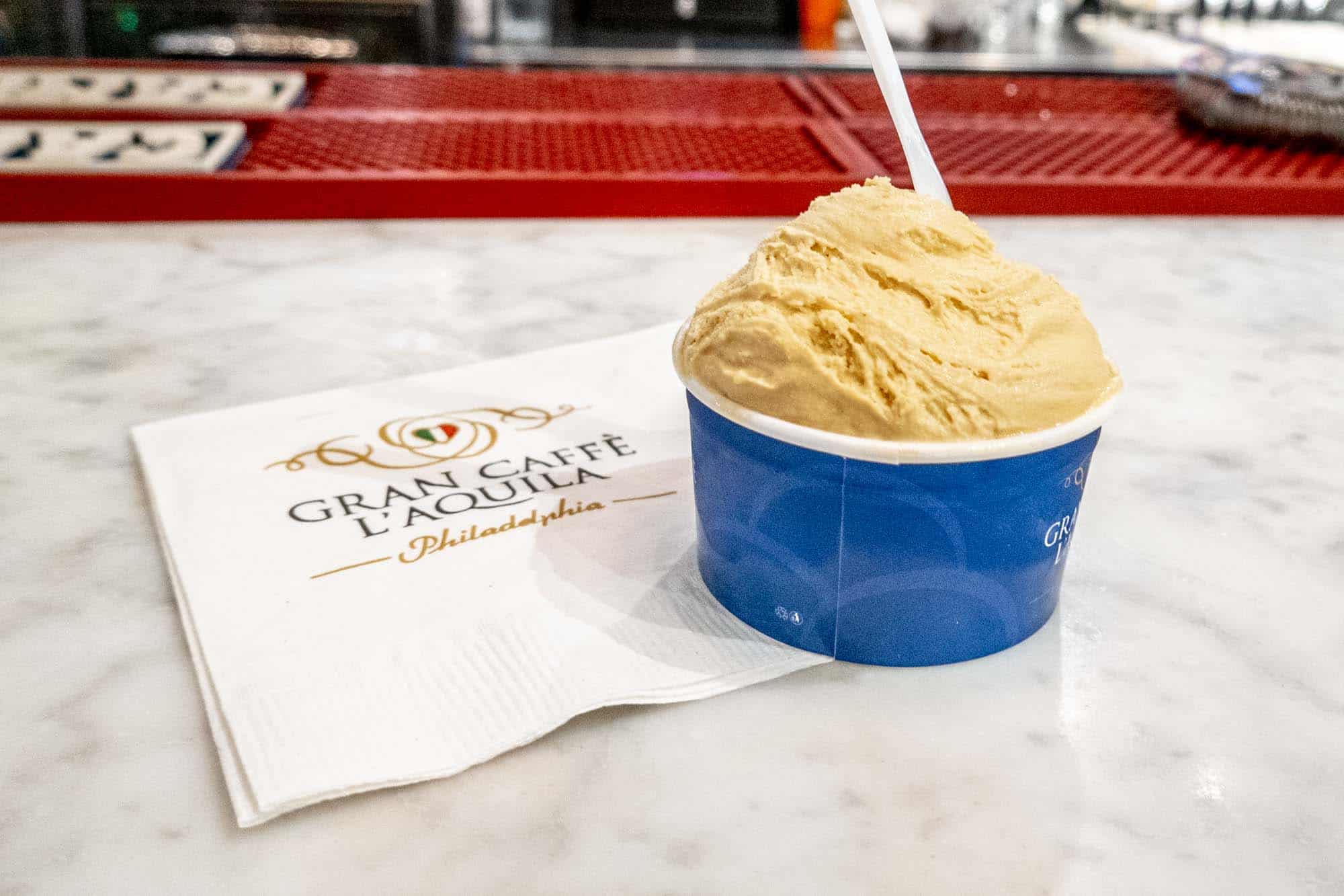 Cup of gelato on a counter next to a napkin that reads "Gran Caffe L'Aquila Philadelphia"