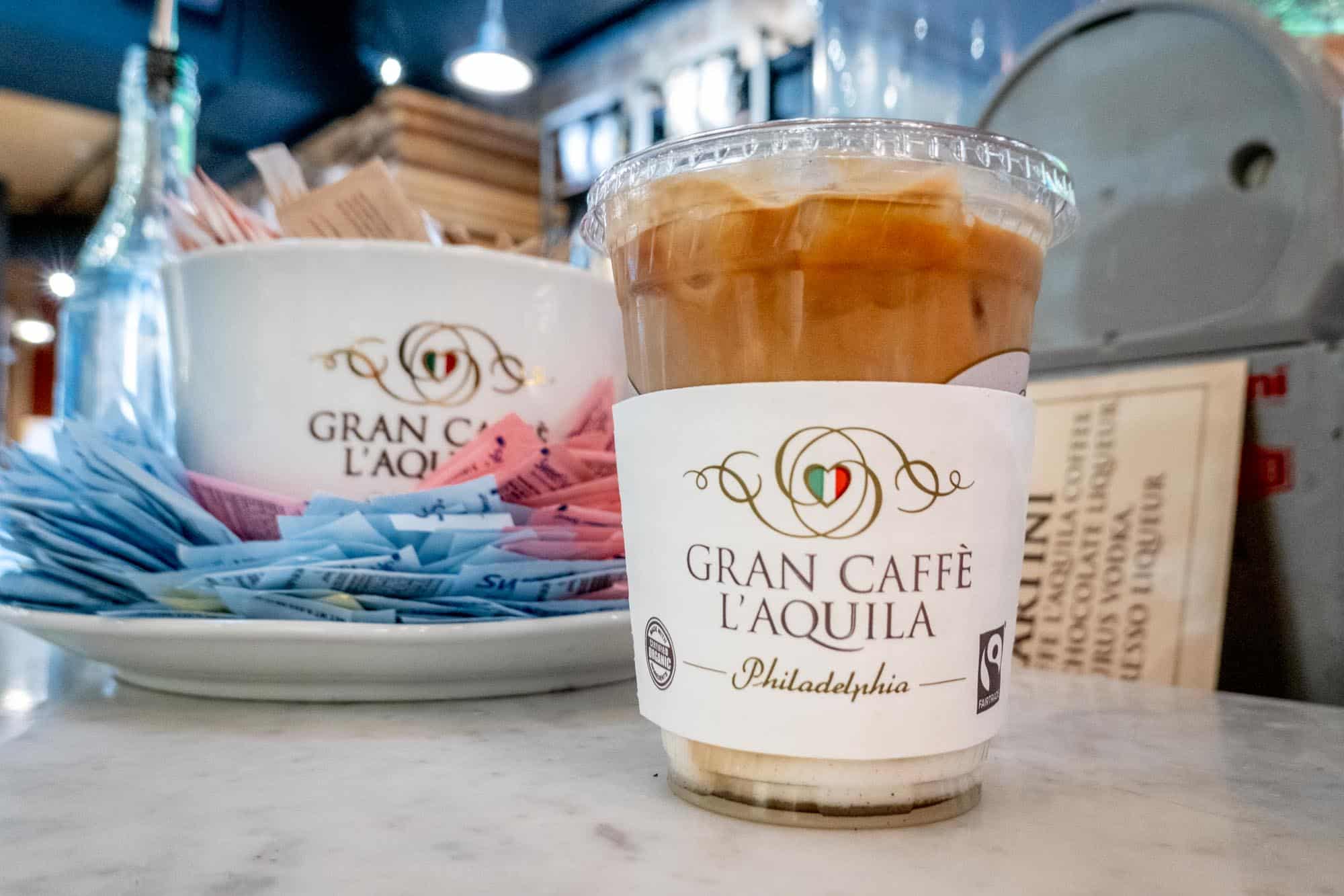 Cup of iced coffee on a counter with a sleeve labeled "Gran Caffe L'Aquila: Philadelphia."