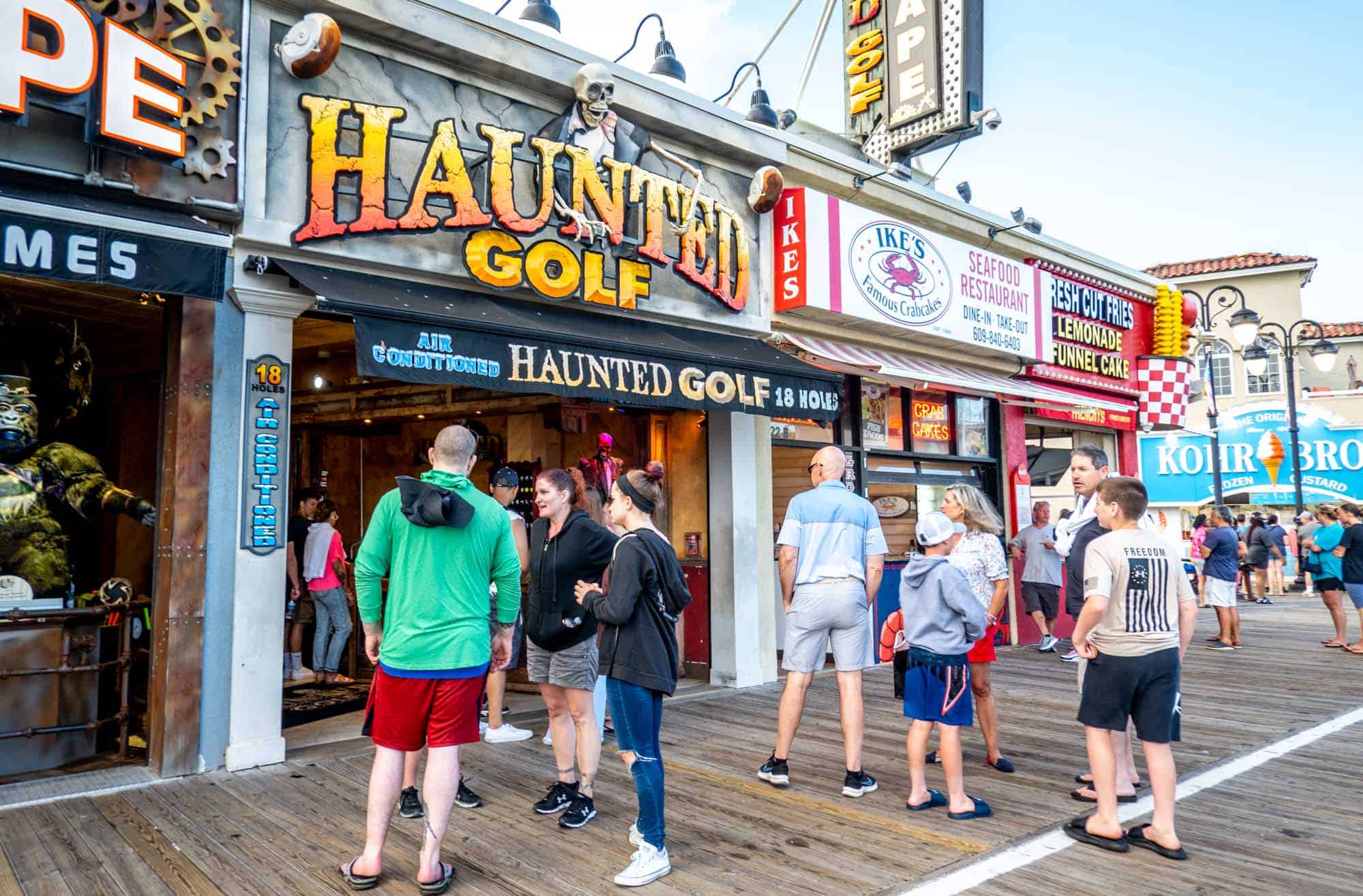 People standing on the boardwalk outside a storefront with a sign for "Haunted Golf"