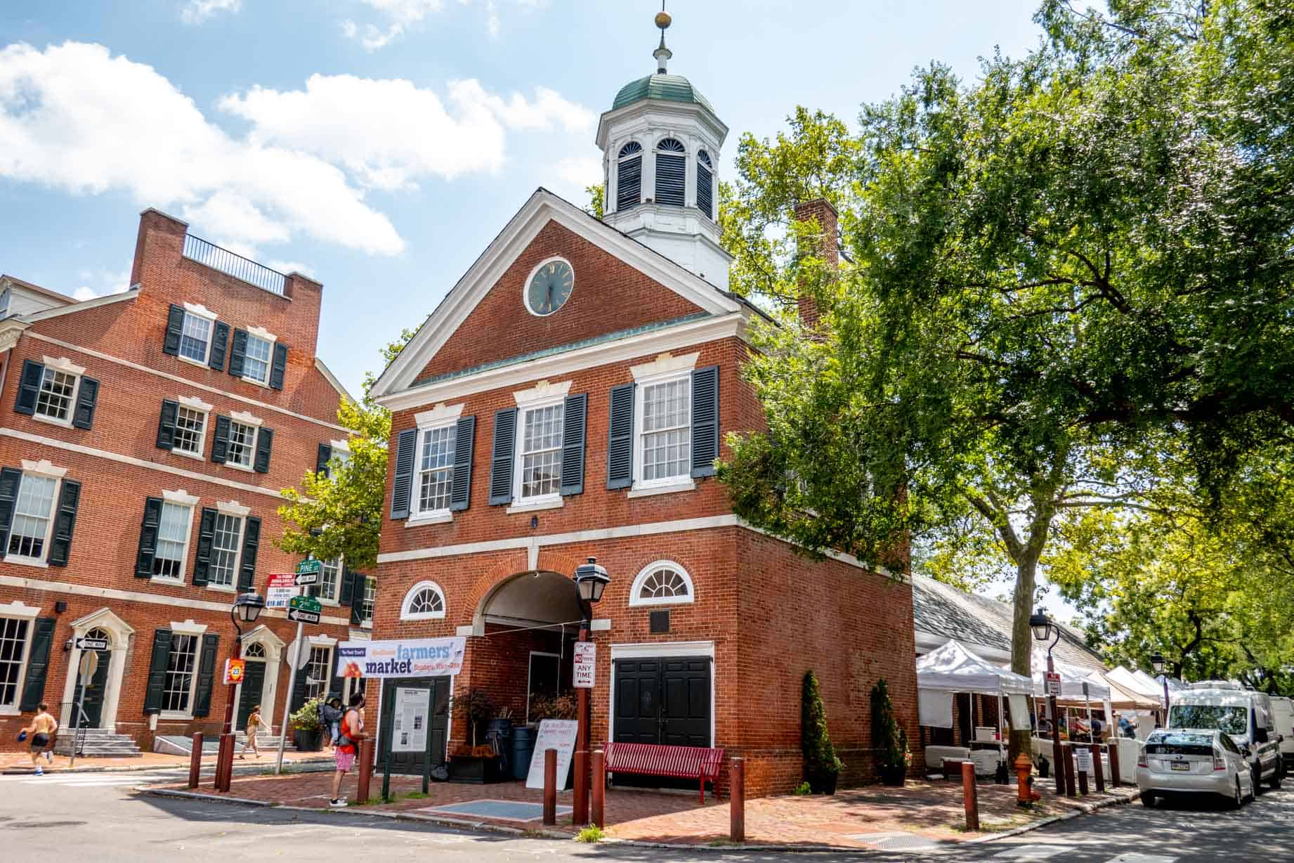 Person in front of a brick building with an arched doorway and cupola.