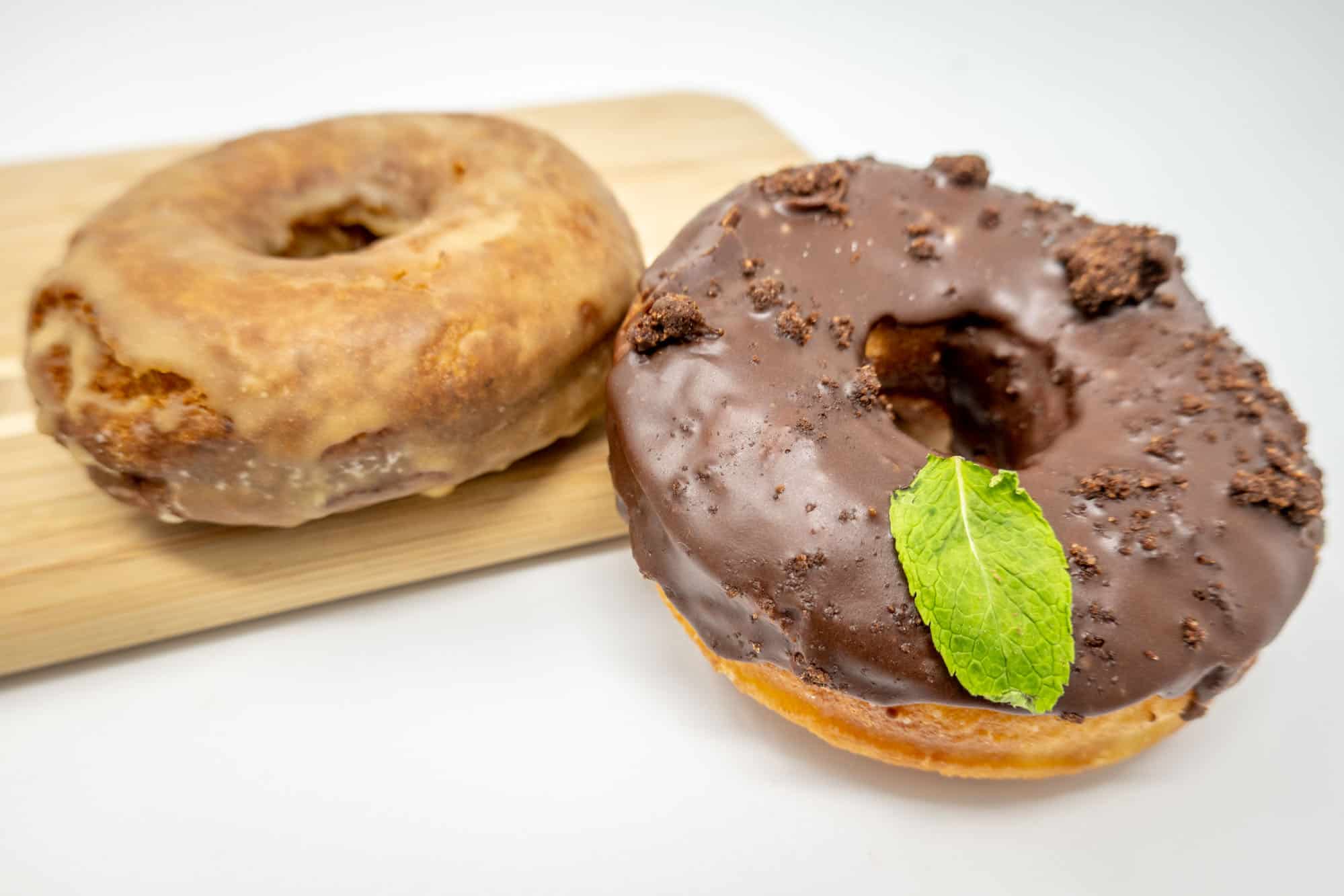 One glazed donut and one chocolate donut topped with a mint leaf.