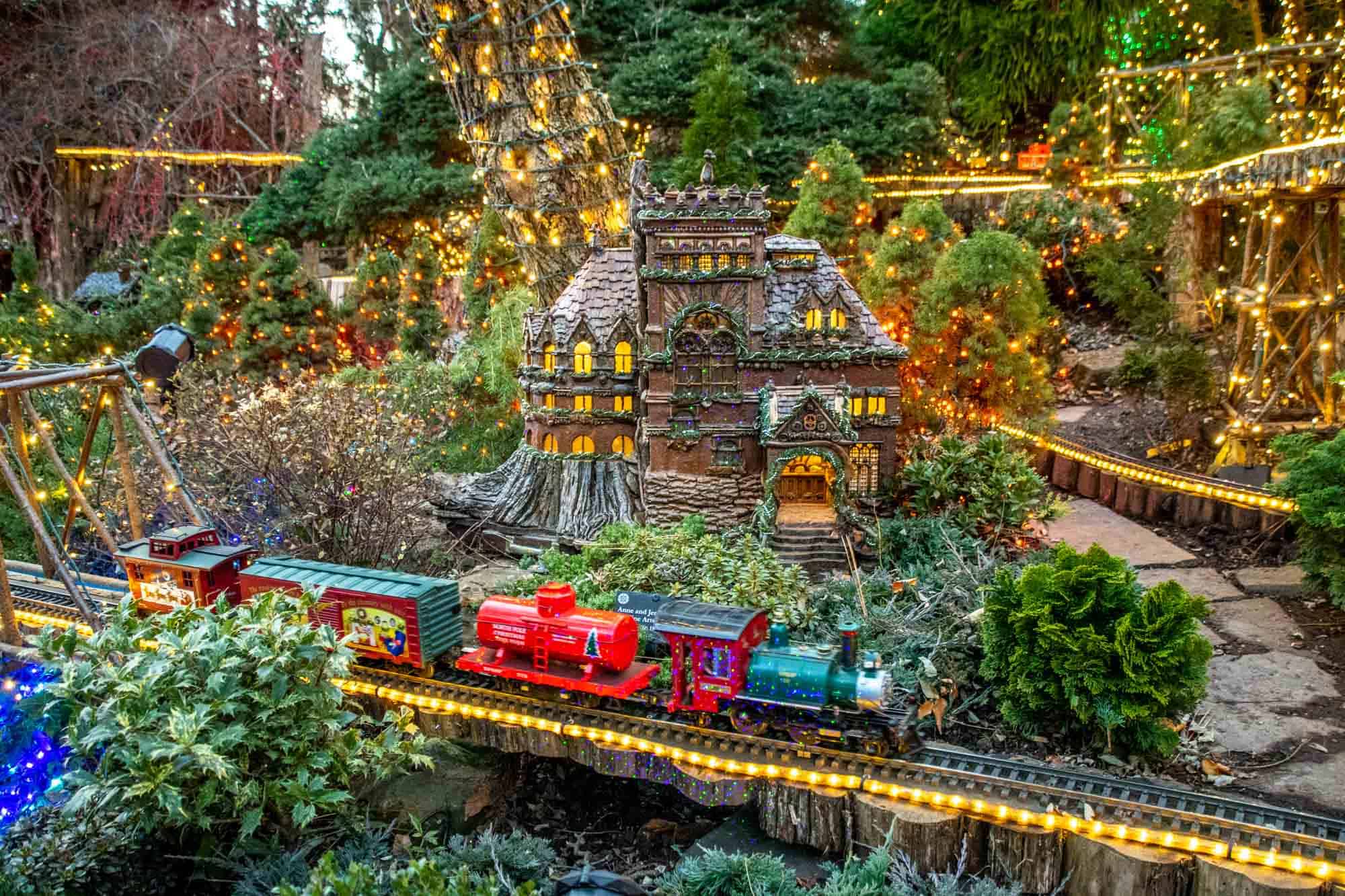 Model train going through scenery lit with Christmas lights.