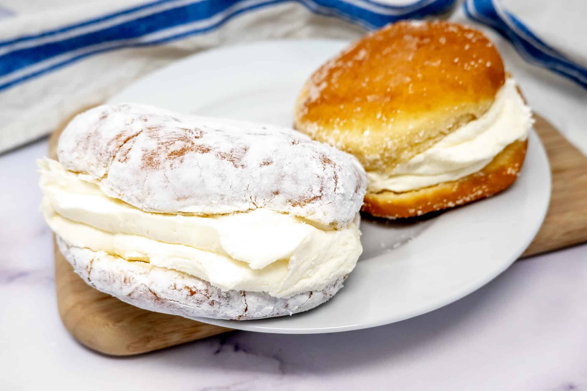 Two cream-filled donuts on a plate--one topped with powdered sugar and the other with granulated sugar