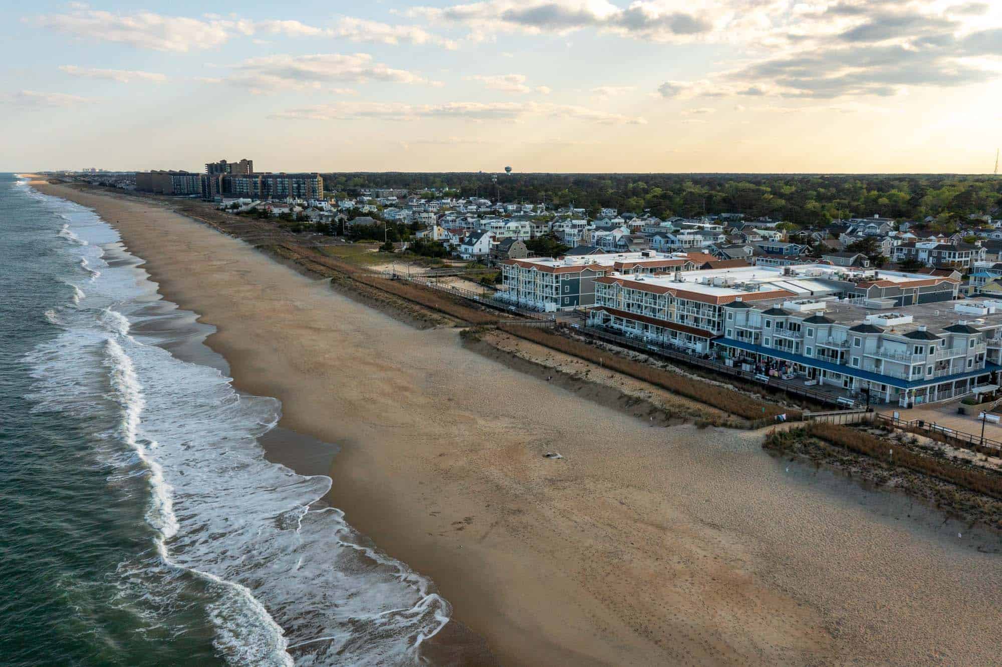 Aerial view of waves hitting a Delaware beach in front of a boardwalk, businesses, and homes.