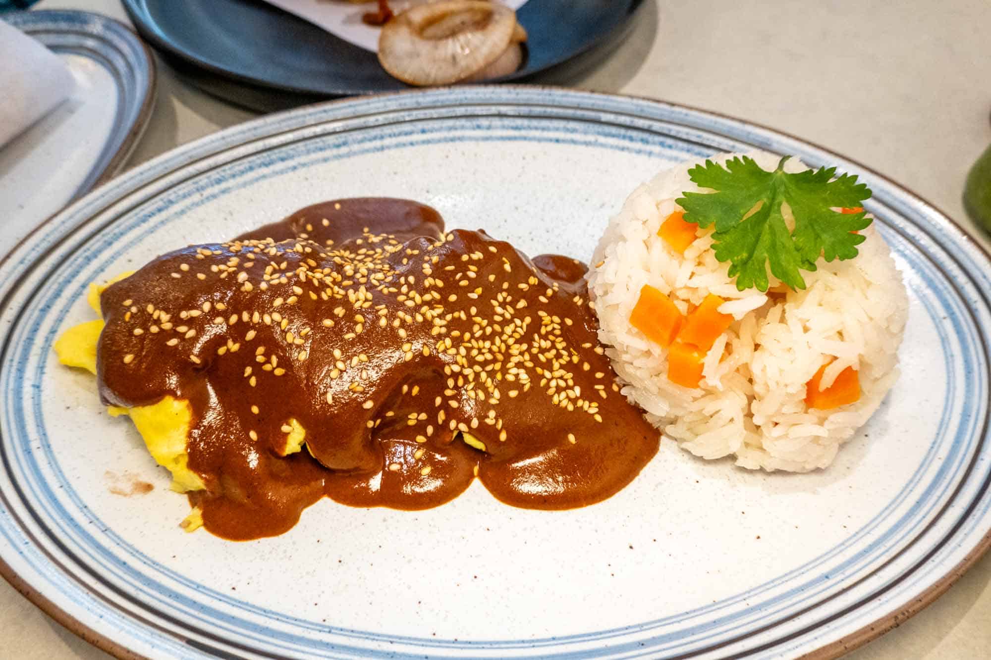 Scrambled eggs covered with mole next to rice on a plate.