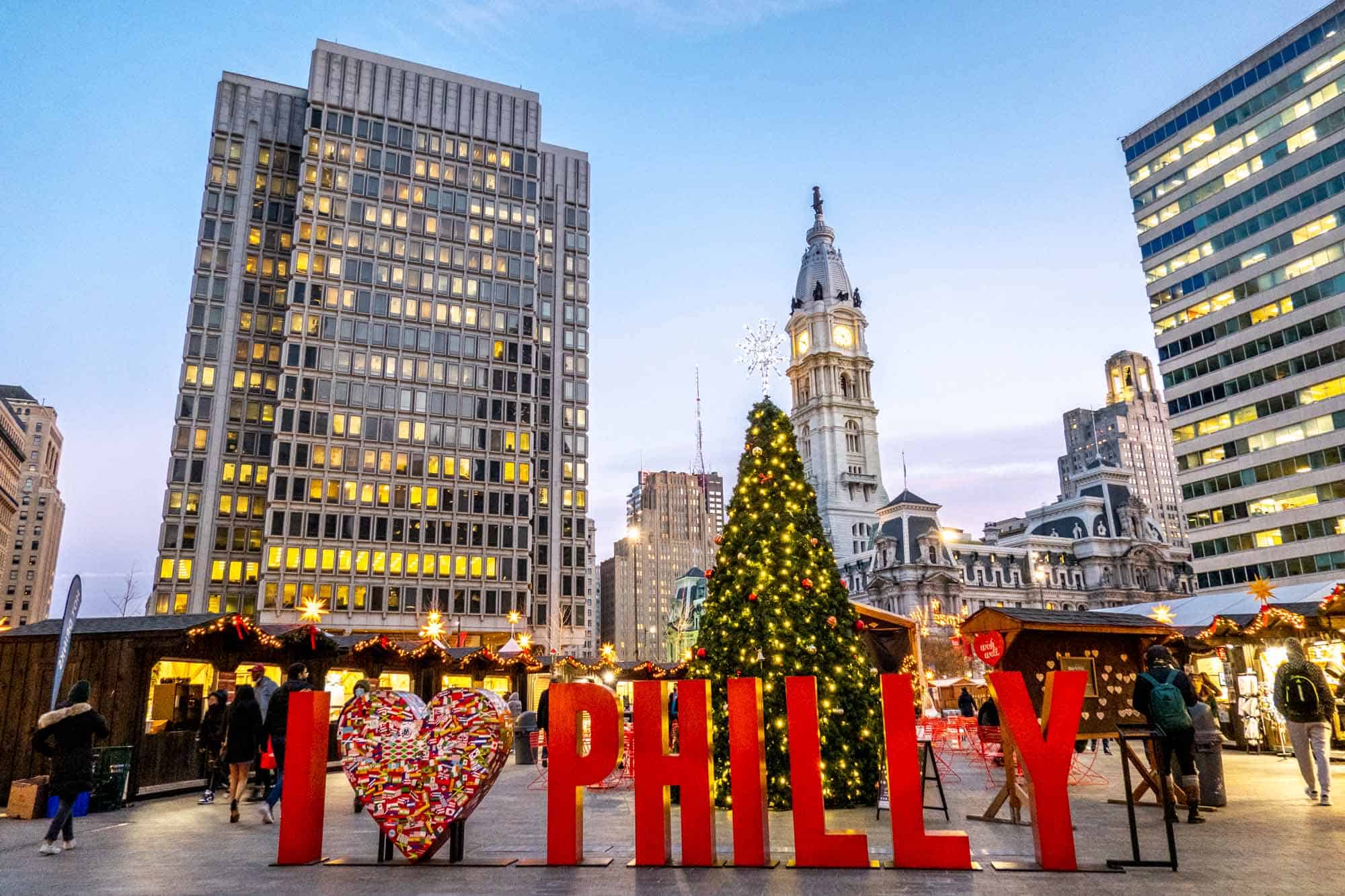 I Heart Philly sign in front of a Christmas tree surrounded by Christmas market stalls.