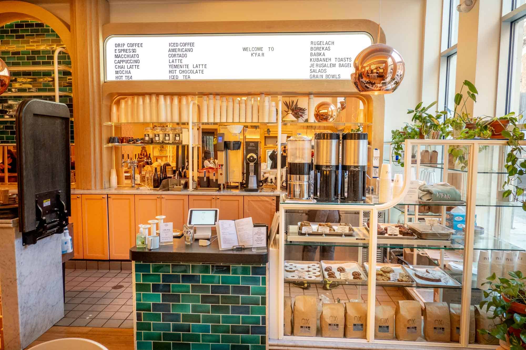 Coffee counter with cups, carafes, and pastries and a light board menu on the wall.