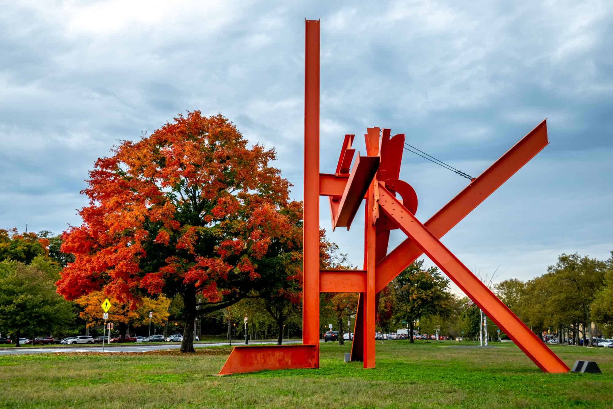 Bright red maple tree beside an abstract sculpture made from red steel.