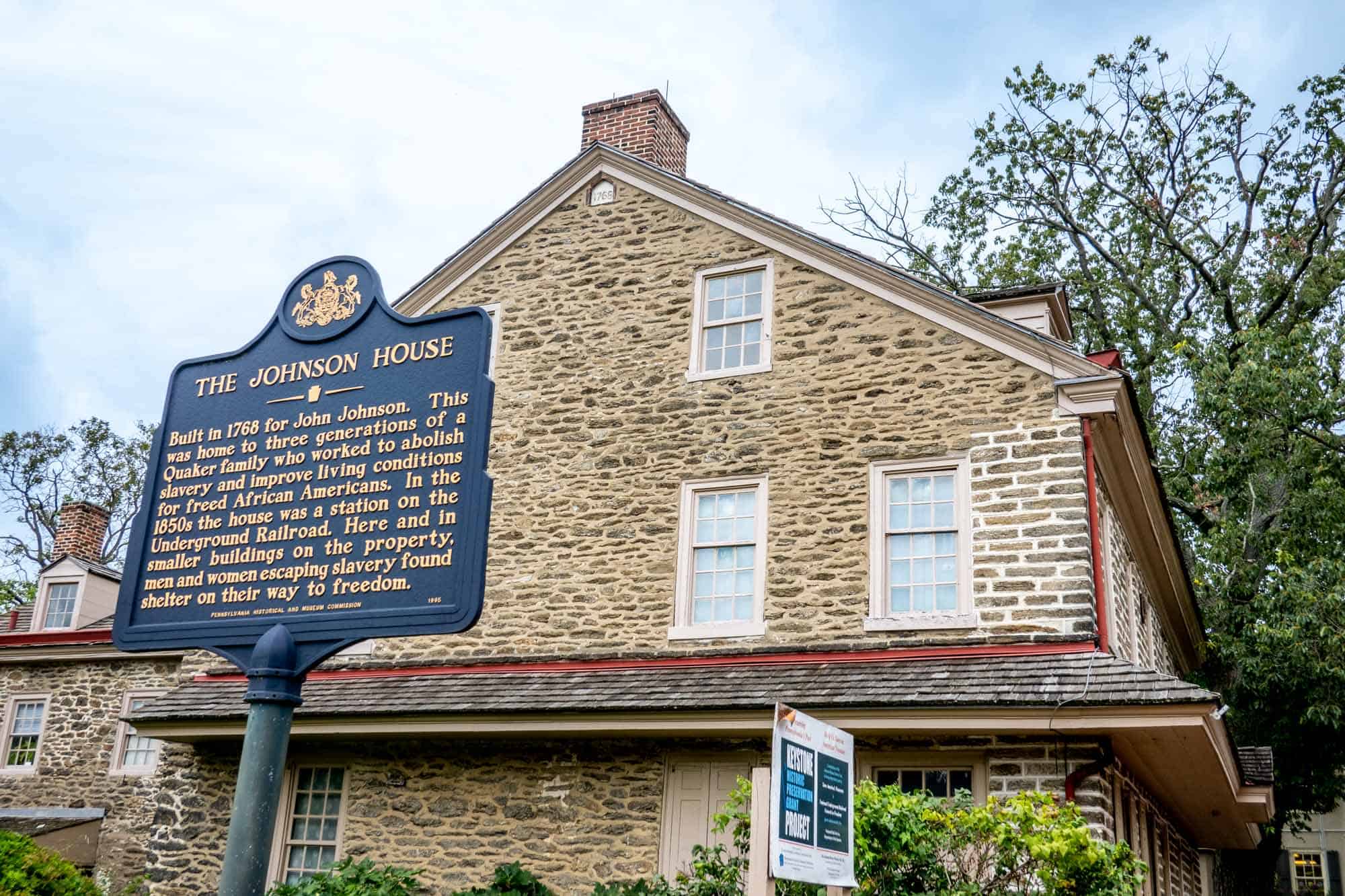 Stone building with an historical sign: "The Johnson House. Built in 1768 for John Johnson. This was home to three generations of a Quaker family who worked to abolish slavery and improve living conditions for freed African Americans. In the 1850s the house was a station on the Underground Railroad. Here and in smaller buildings on the property, men and women escaping slavery found shelter on their way to freedom." 