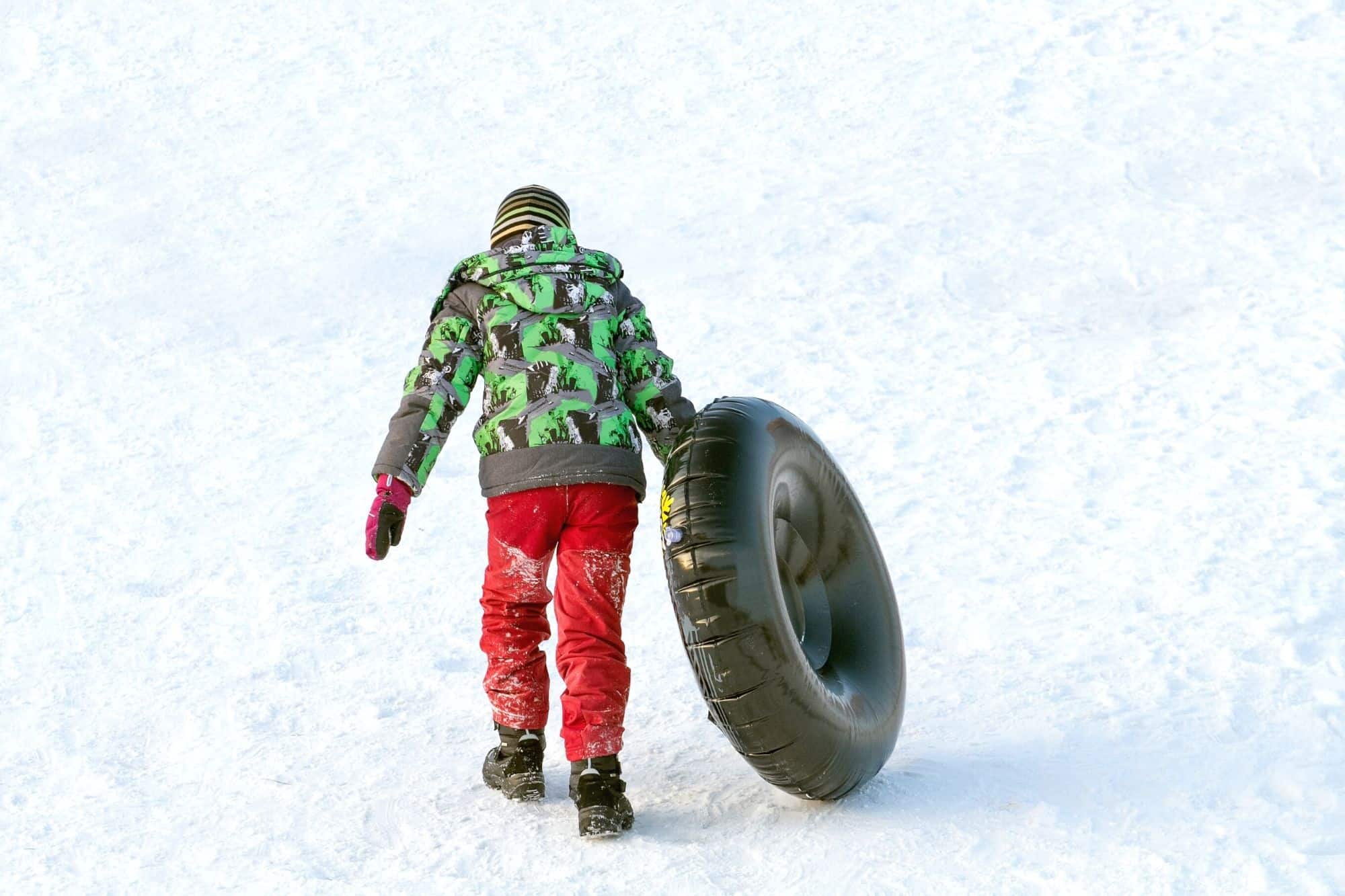 Child walking on snow with inner tube