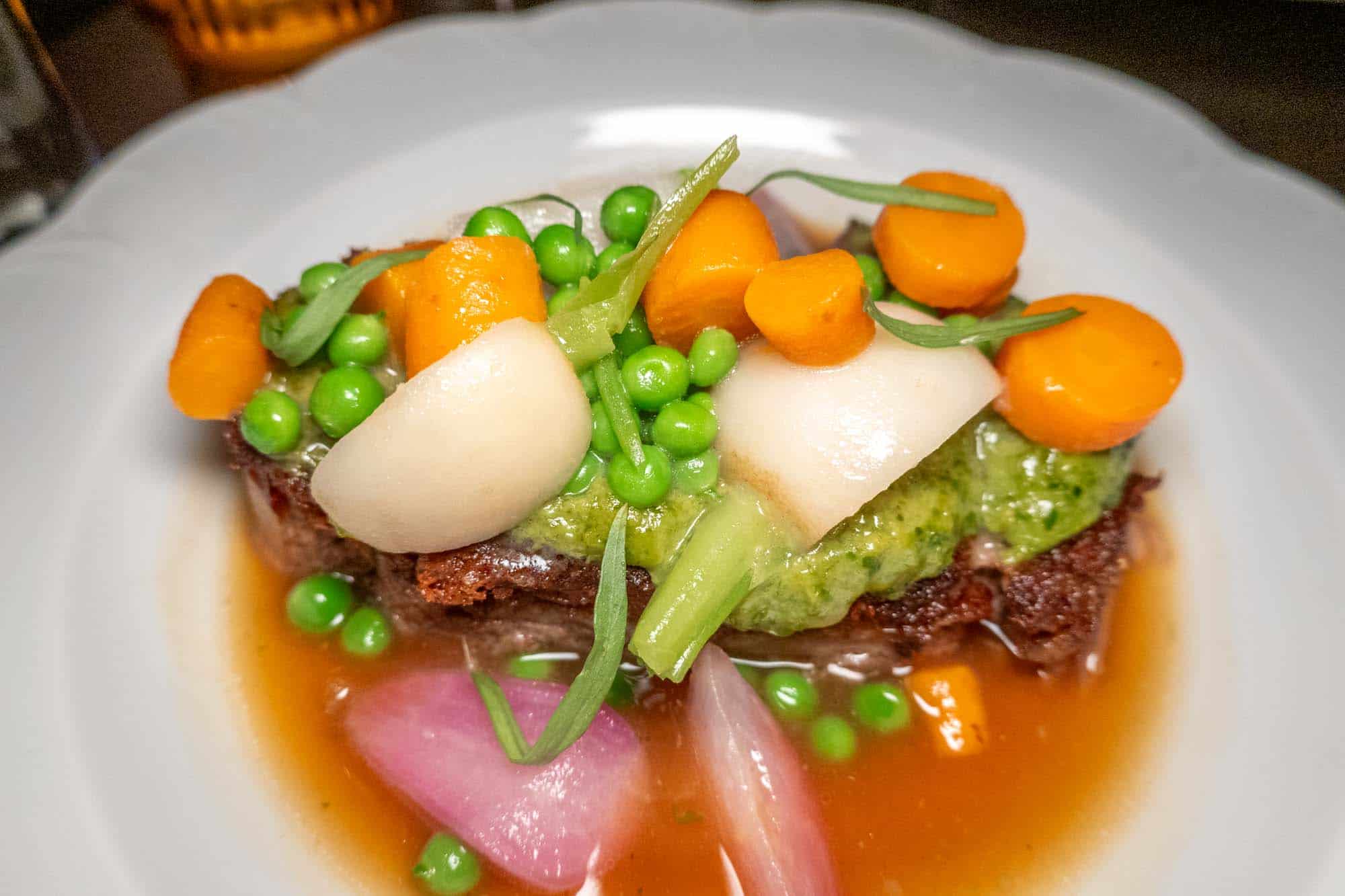 Roasted lamb shoulder topped with turnips, carrots, peas and shallots
