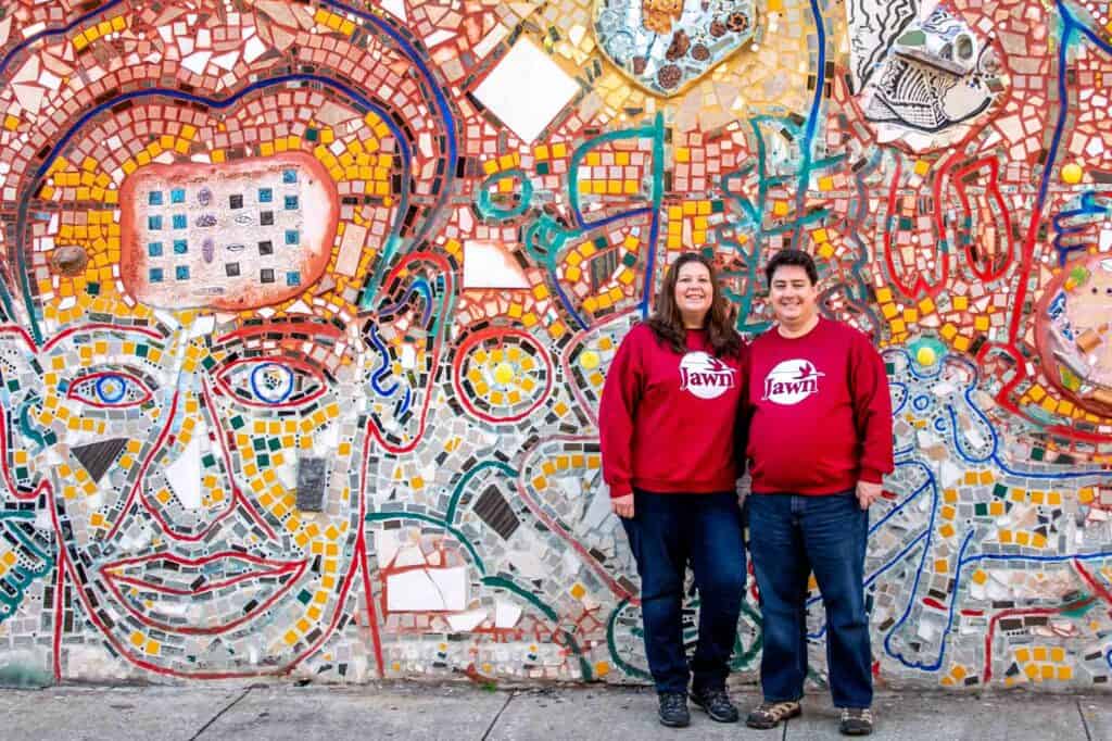 Woman and man wearing red sweatshirts standing in front of a wall mosaic