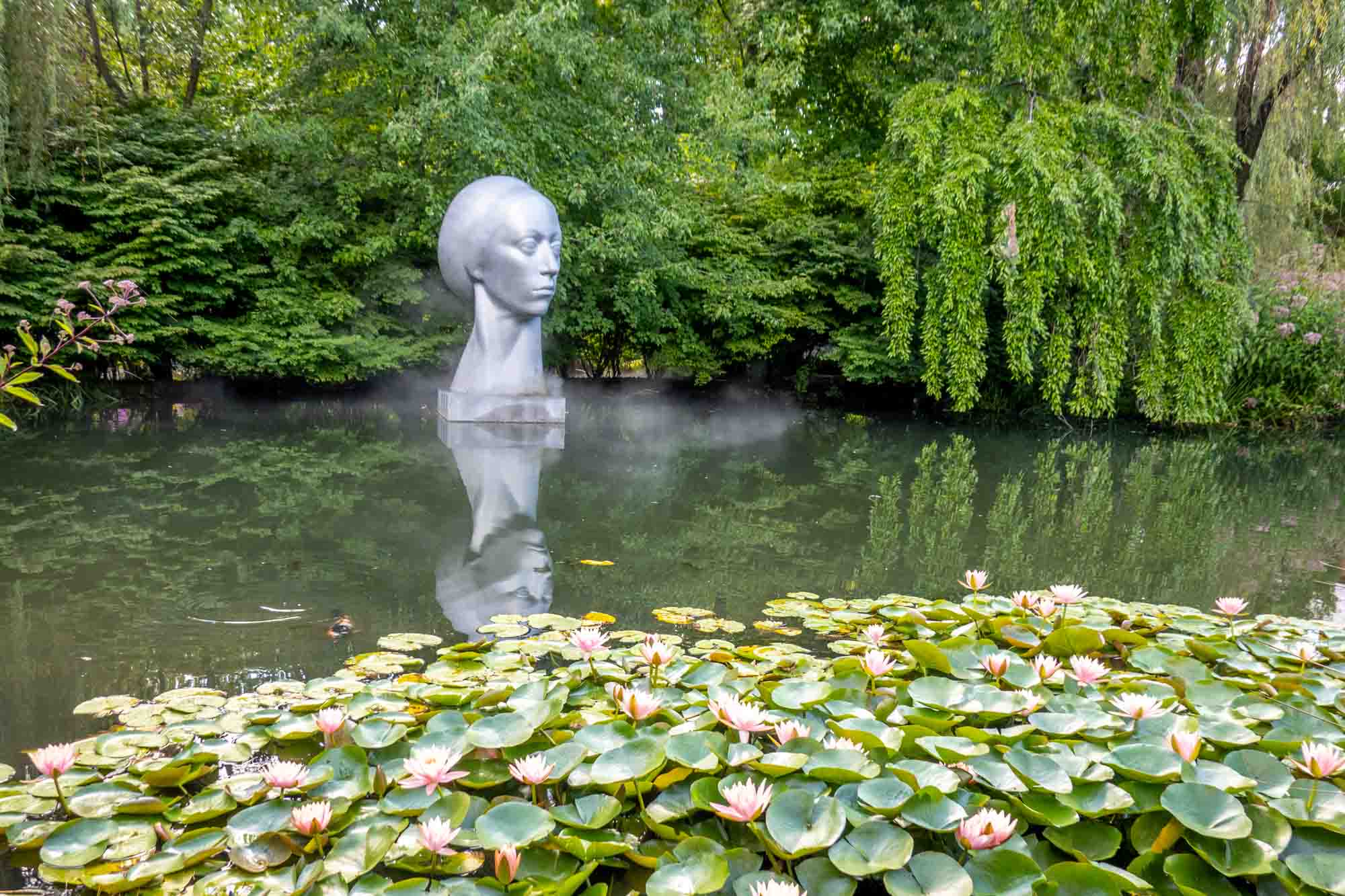 Sculpture of a woman's head in a pond with water lilies.