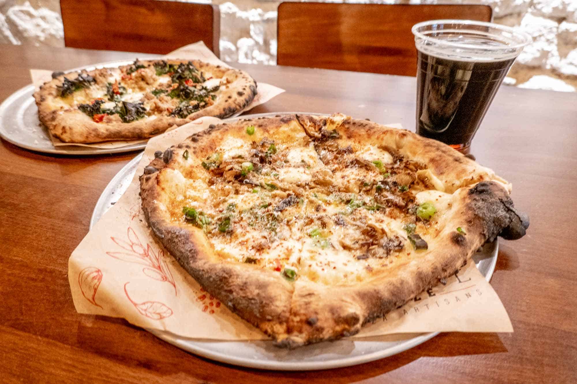 Two pizzas and a glass of dark beer on a table