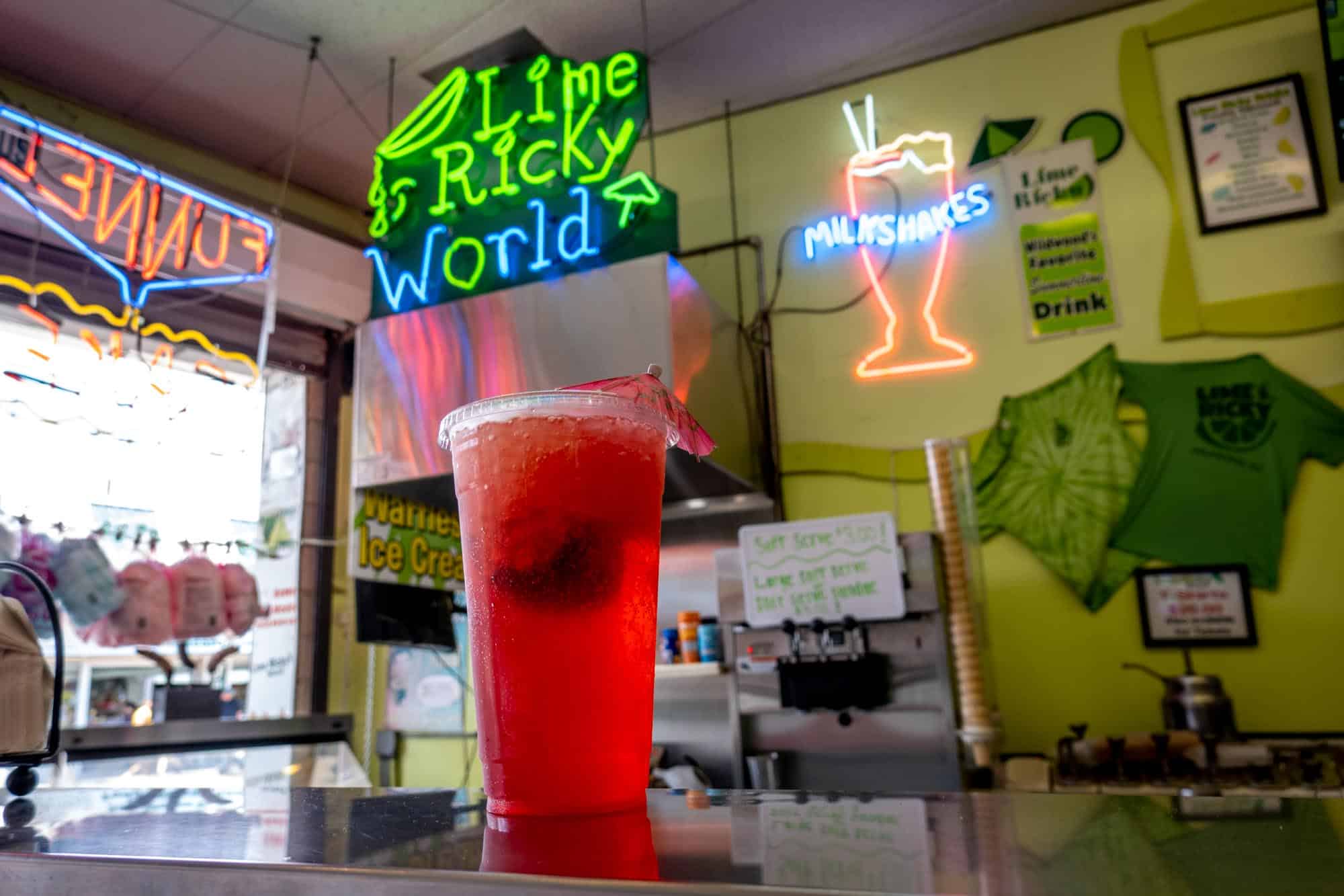 Red drink on counter in front of neo sign saying "Lime Ricky World"