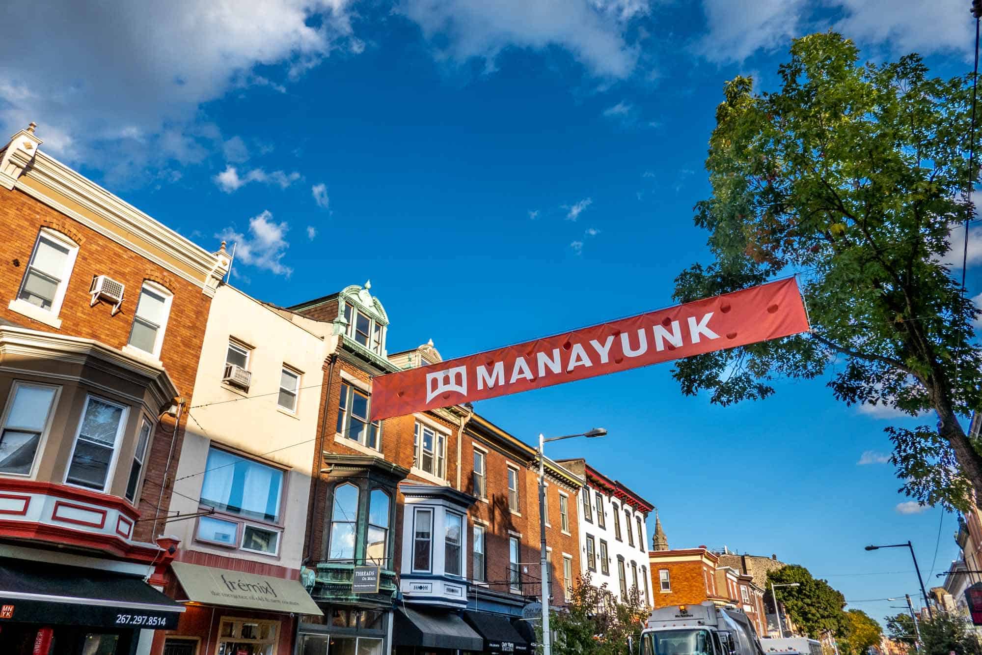 Sign reading "Manayunk" over a cute street lined with businesses.