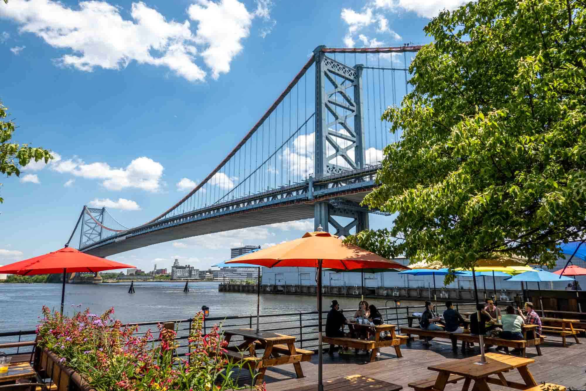 Colorful picnic tables on a pier with beside a bridge.