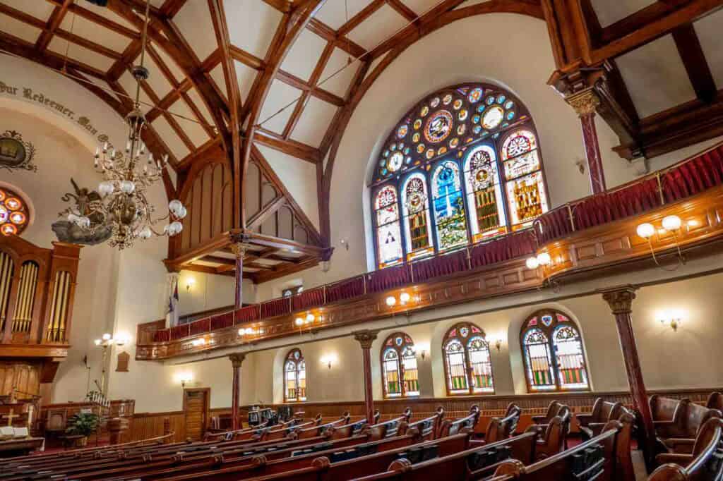 Wooden pews, a chandelier, and stained glass windows inside the historic sanctuary of Mother Bethel AME Church.