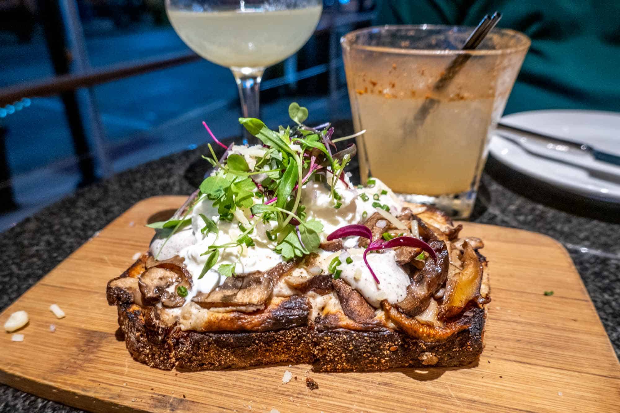 Toast with mushrooms and burrata on a wood serving board.