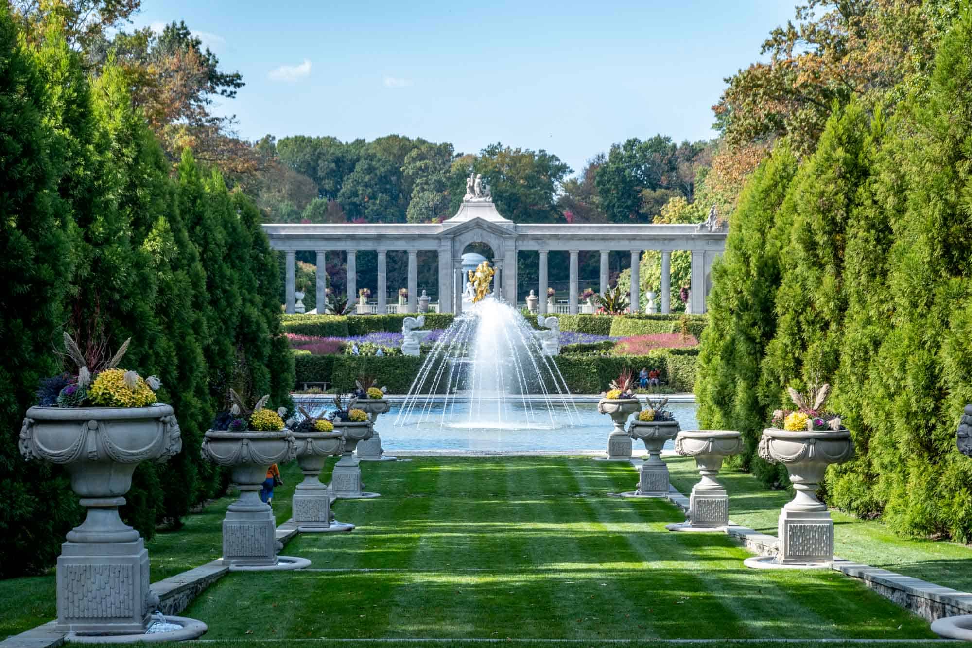 Grand fountain at the end of a grass path lined by statues