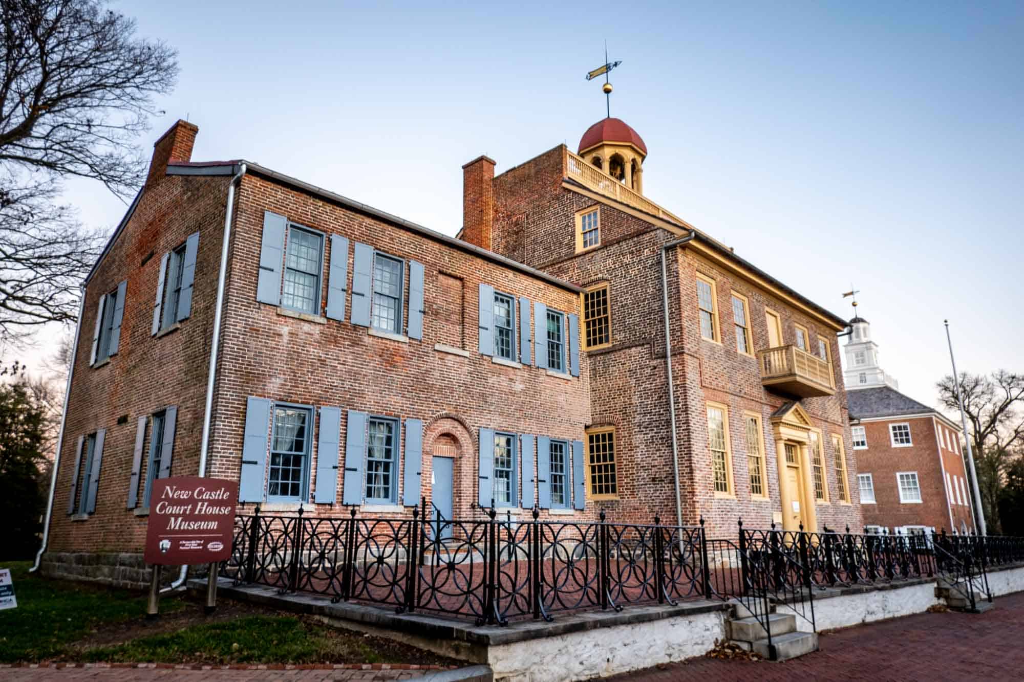 Brick building with blue and yellow trim beside a sign: "New Castle Court House Museum."