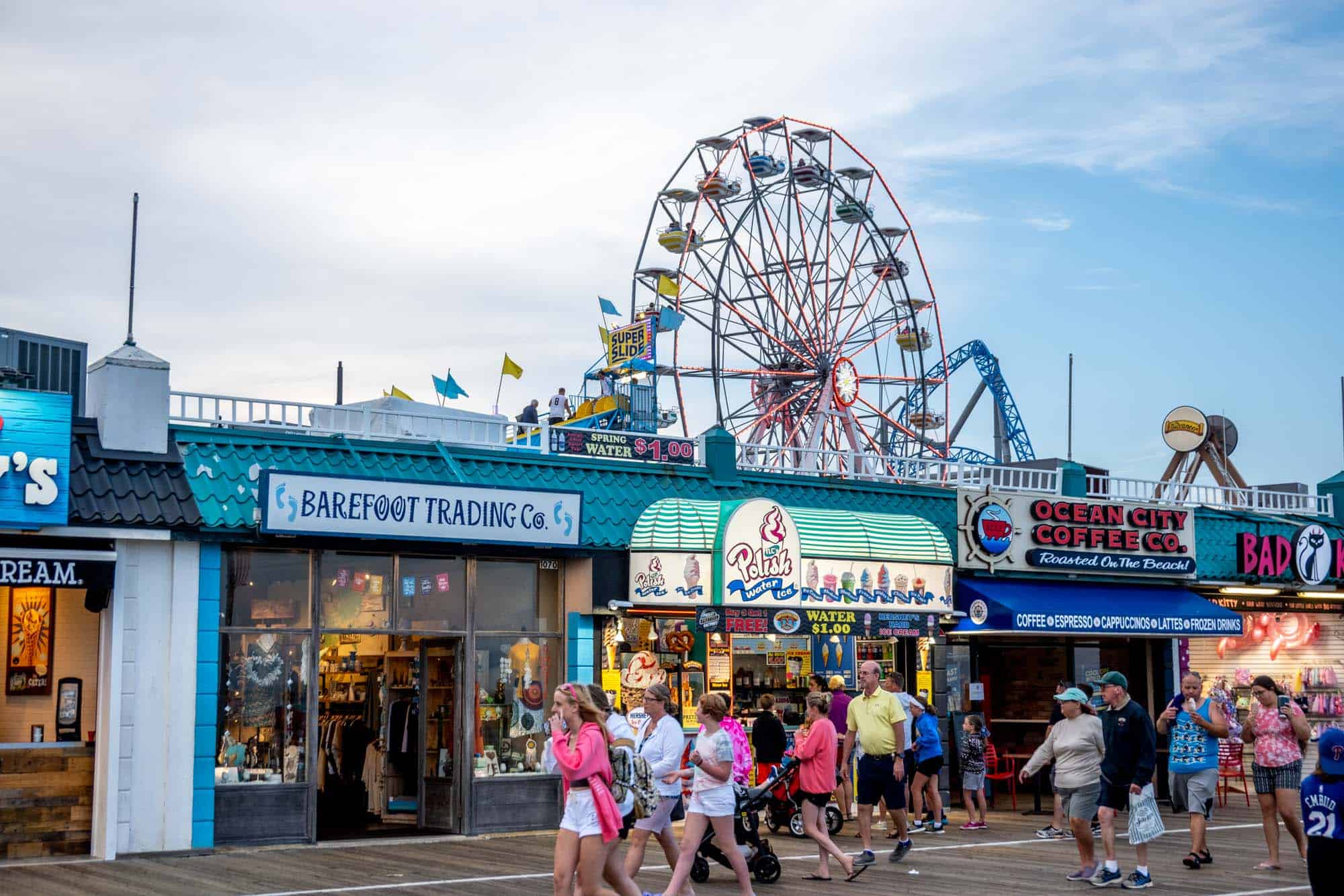 Ferris wheel and rides in the background with businesses and people walking on the boardwalk in Ocean City NJ.