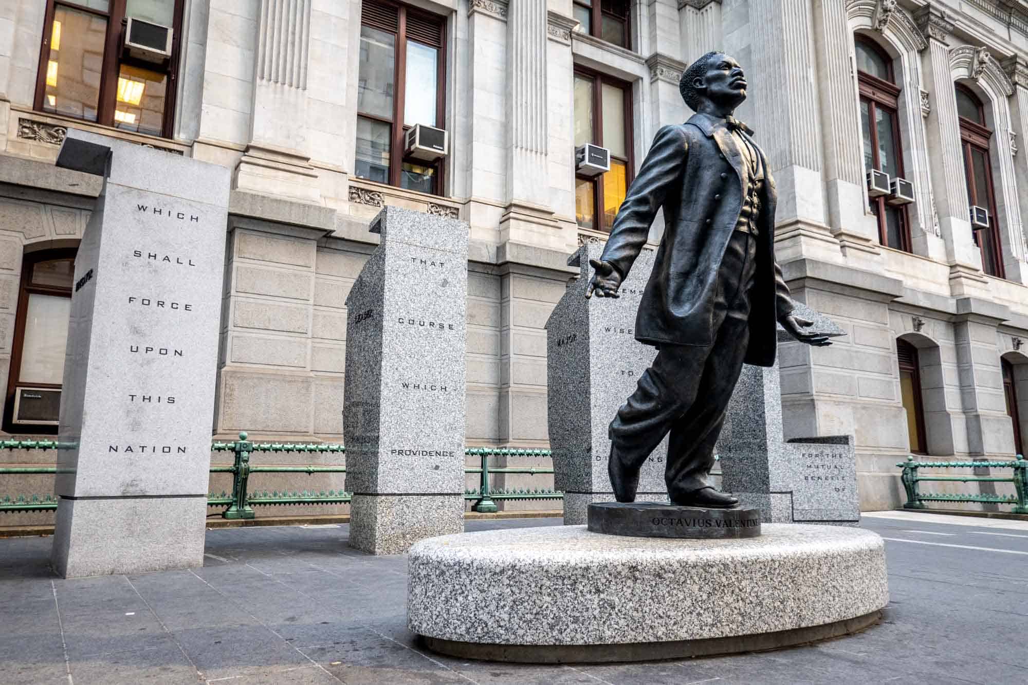 Bronze statue of a Black man in a 3-piece suite in front of four granite blocks
