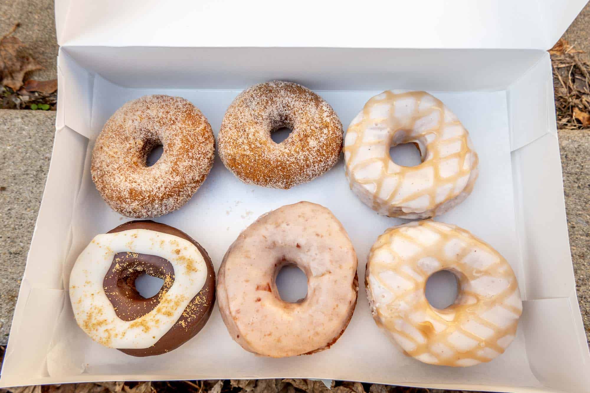 Six donuts topped with sugar and icing in a box.