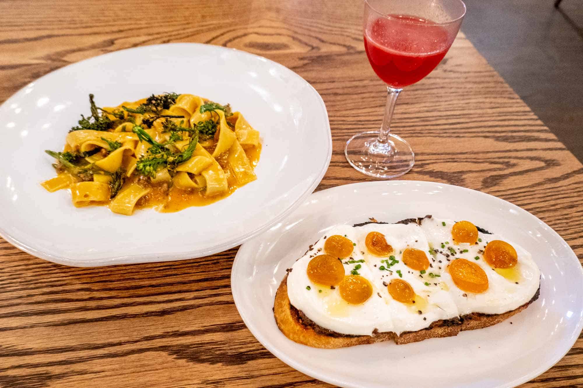 Plate of pasta topped with broccolini next to a plate of cheese-topped toast.