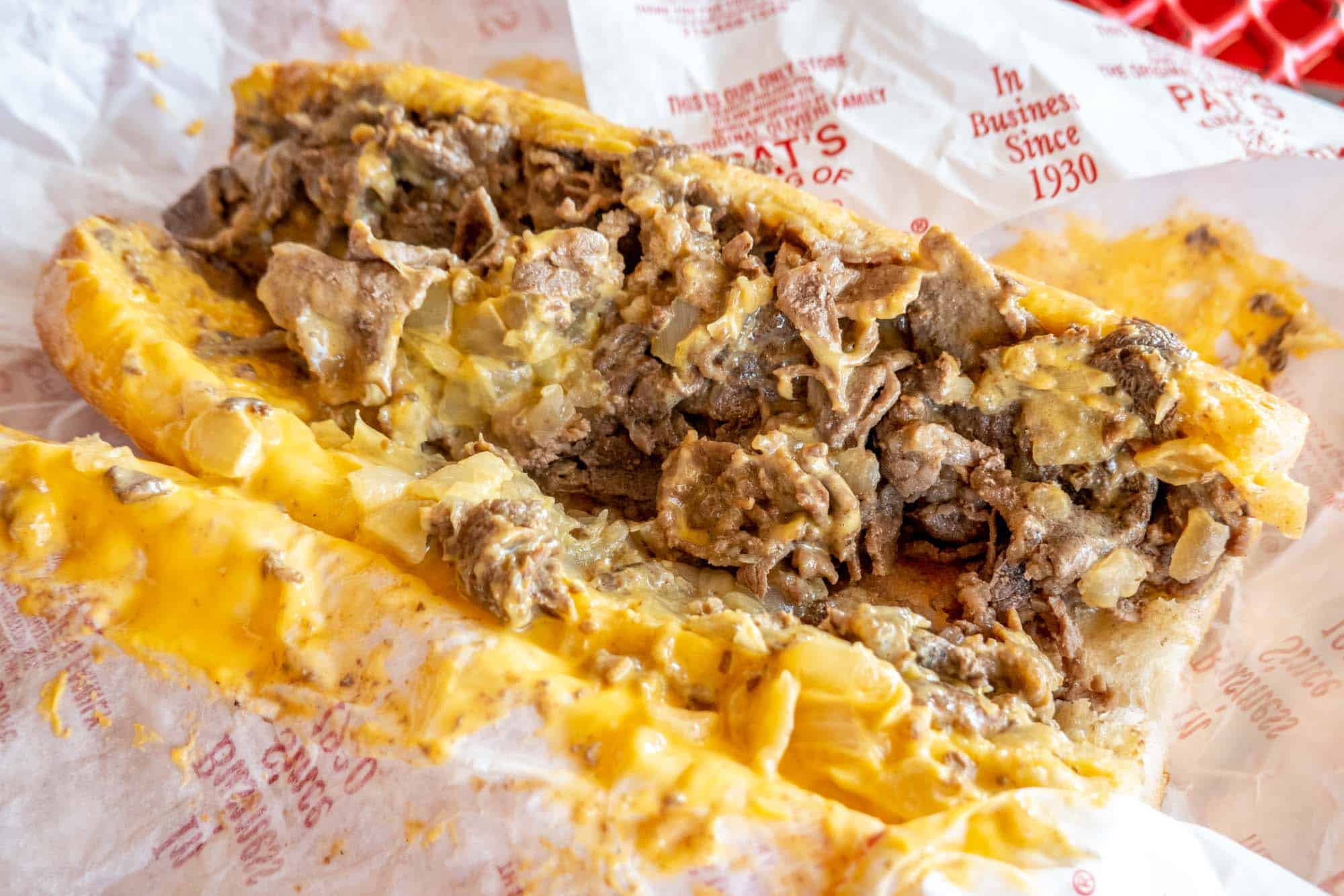 Cheesesteak with yellow cheese on paper wrapper from Pat's King of Steaks.