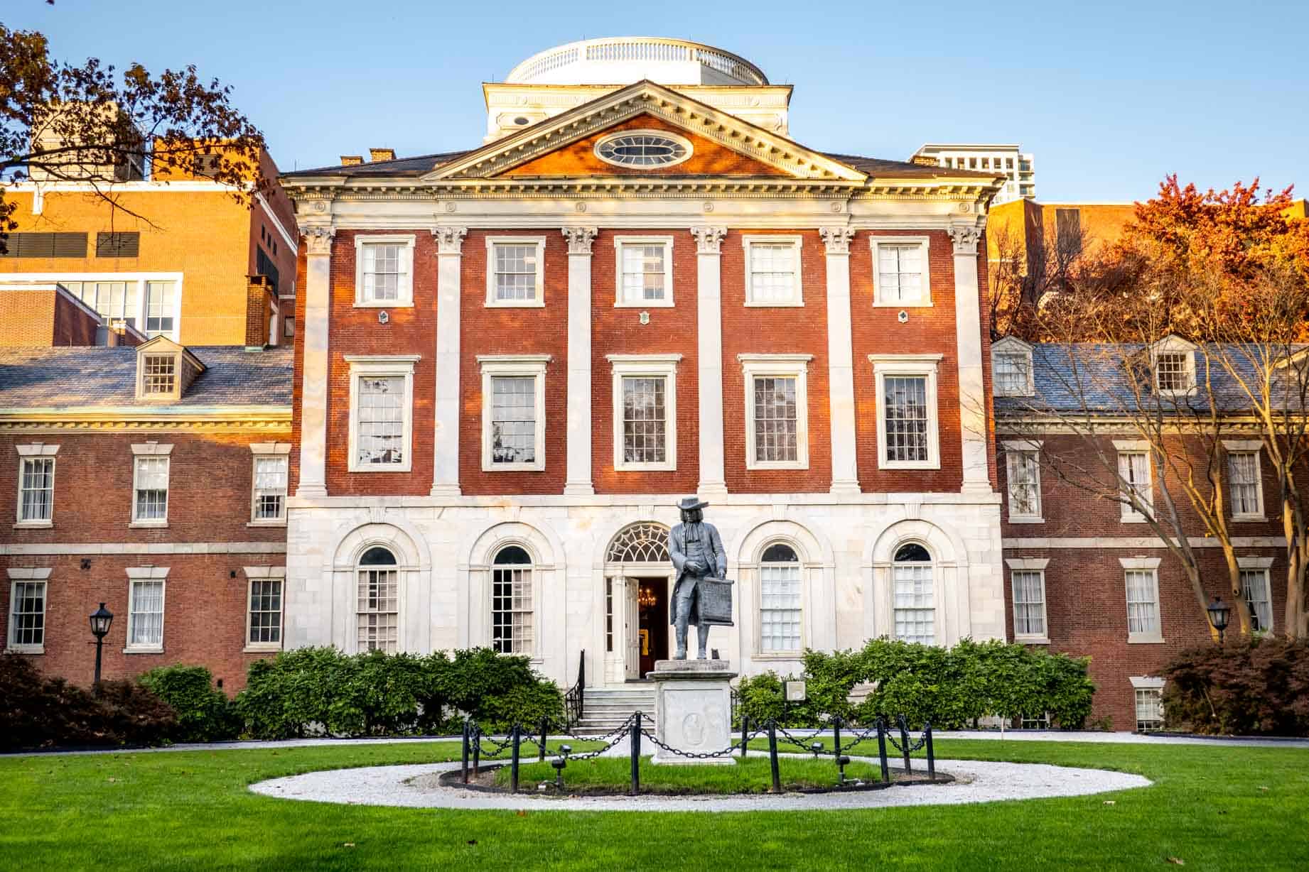 Garden with a statue of a man in the center in front of a brick building.