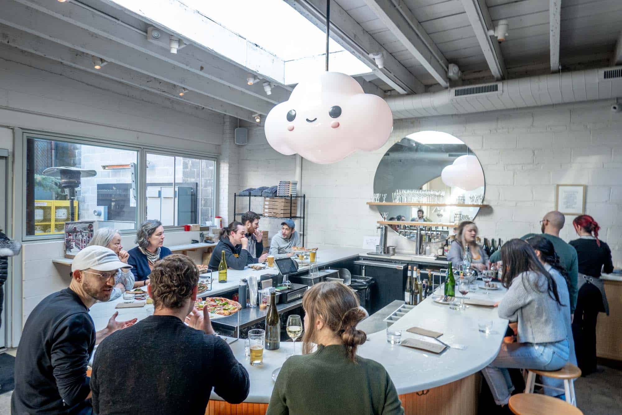 People sitting at a white bar top eating pizza and drinking wine