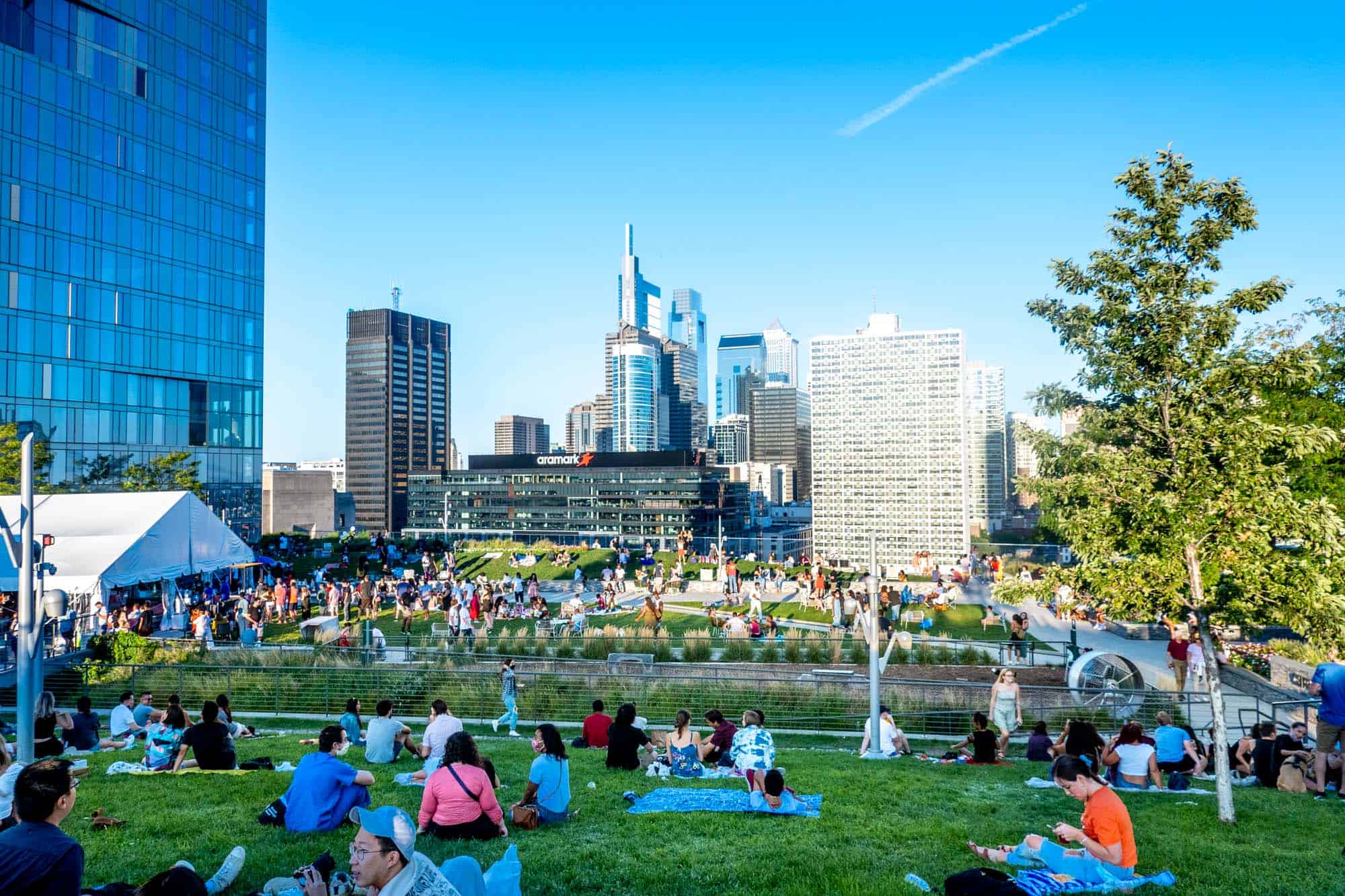 People sitting on the lawn at a rooftop park with a view of skyscrapers in the distance.