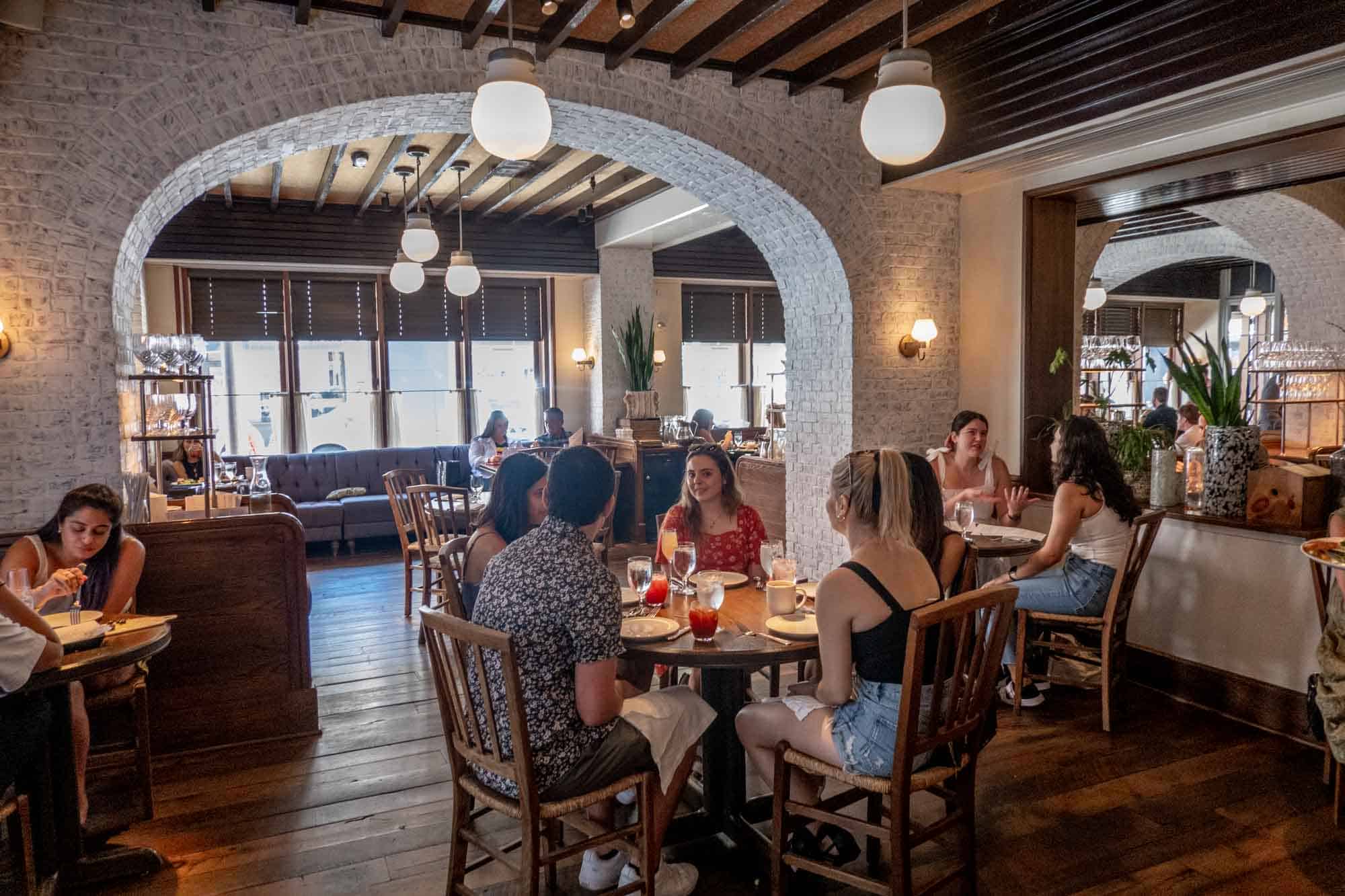 People sitting inside a restaurant with an arched white brick wall.