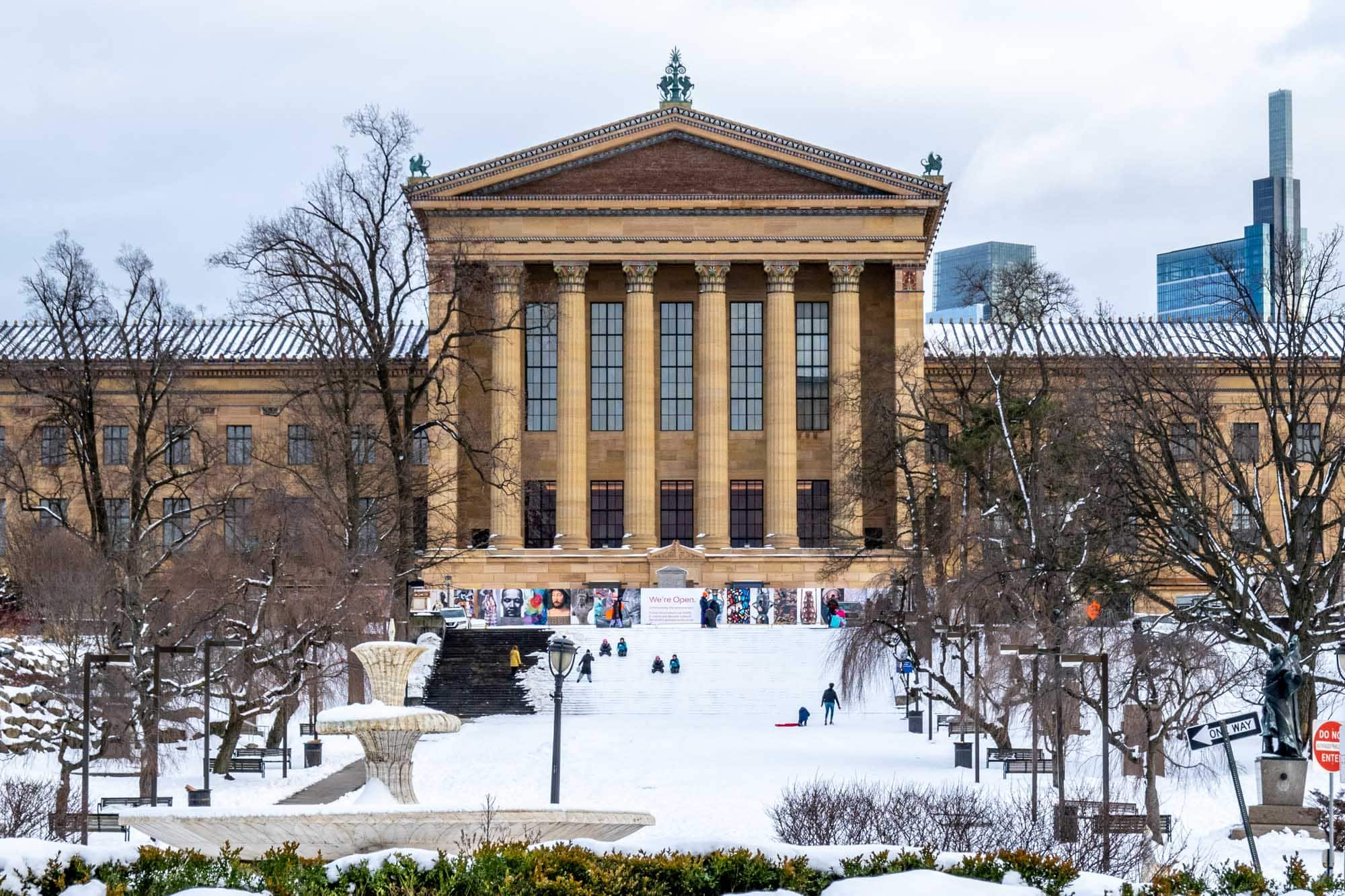 People sledding down the steps of a large building with a colonnaded facade, the Philadelphia Museum of Art. 