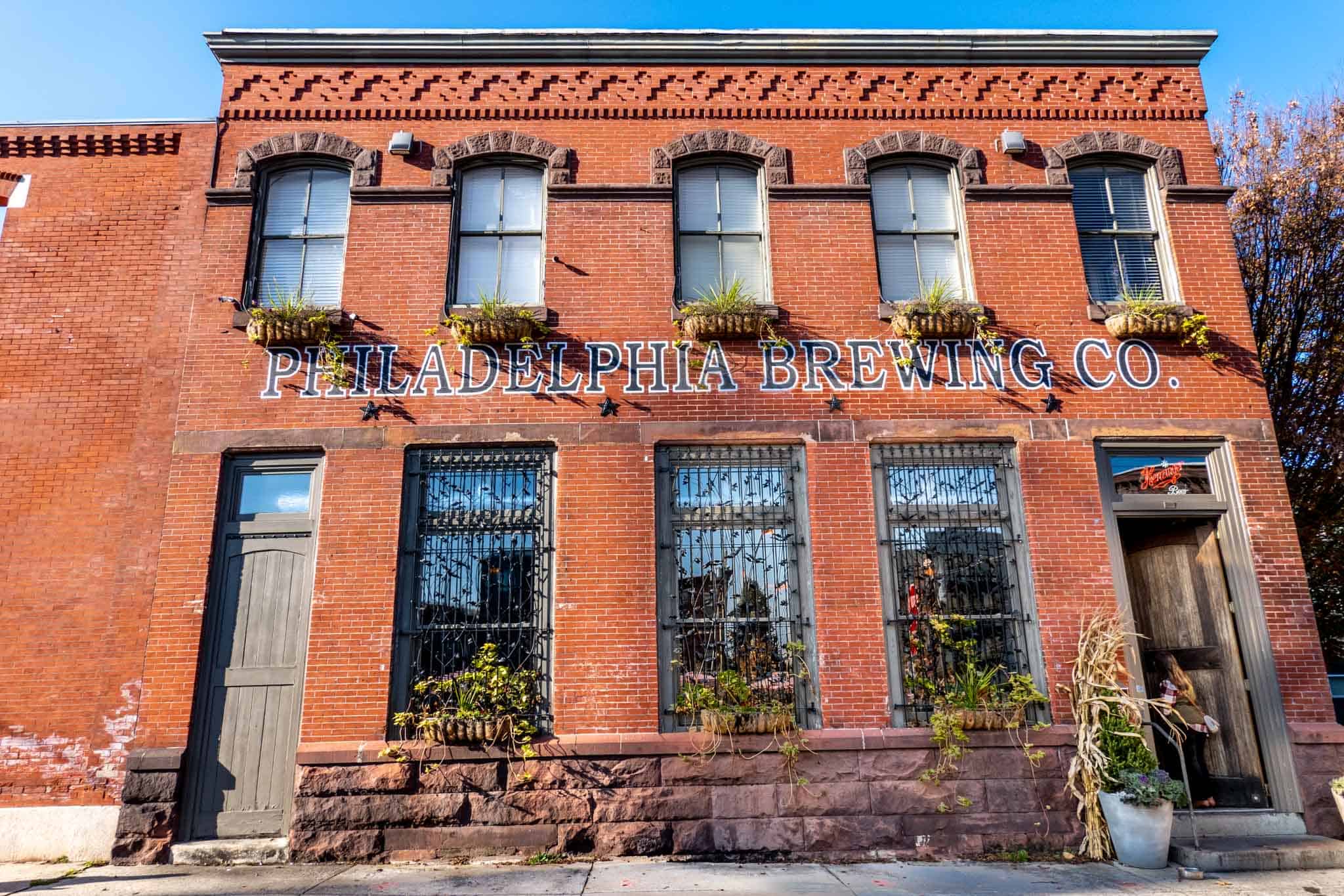 Exterior of a two-story brick building with lots of windows and a painted sign for "Philadelphia Brewing Co."