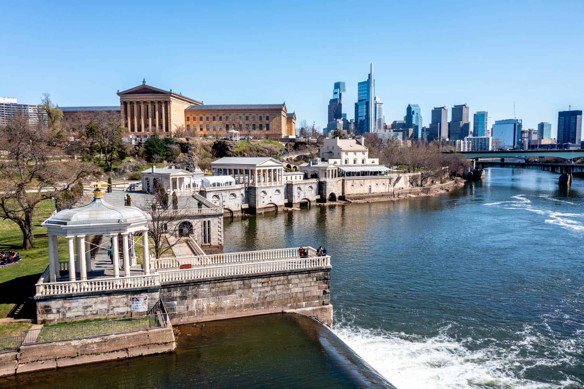 Buildings along a river with a city skyline in the background.