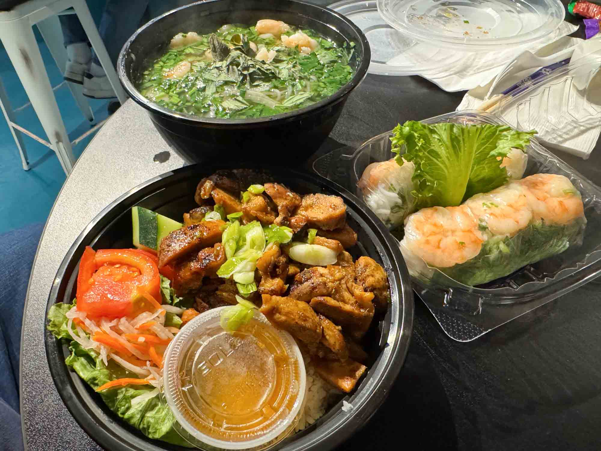 Rice bowl, shrimp spring rolls, and bowl of pho on a table.